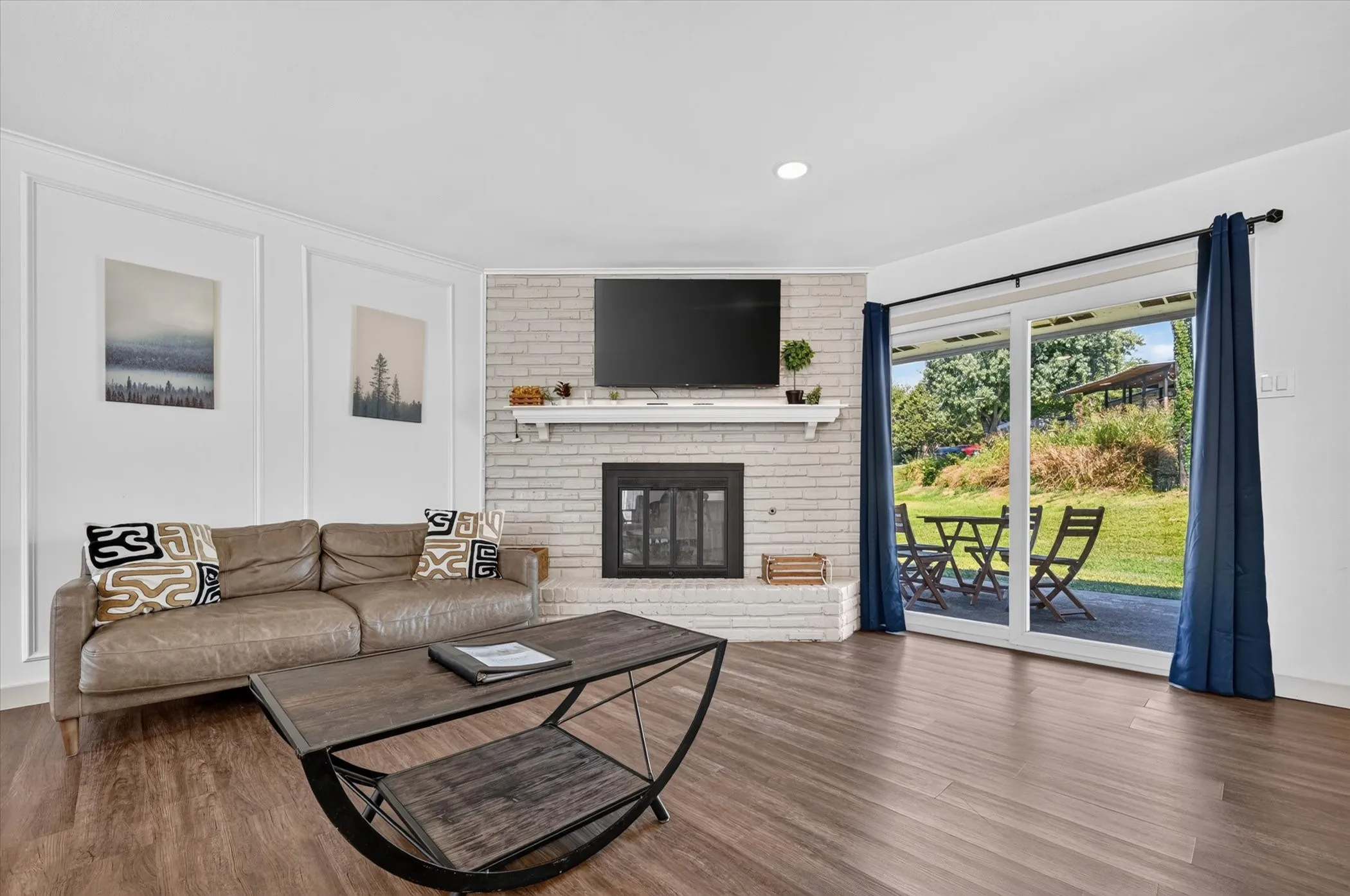 Wood-finish flooring, white brick fireplace with a mantel, recessed lighting, and sliding glass patio doors