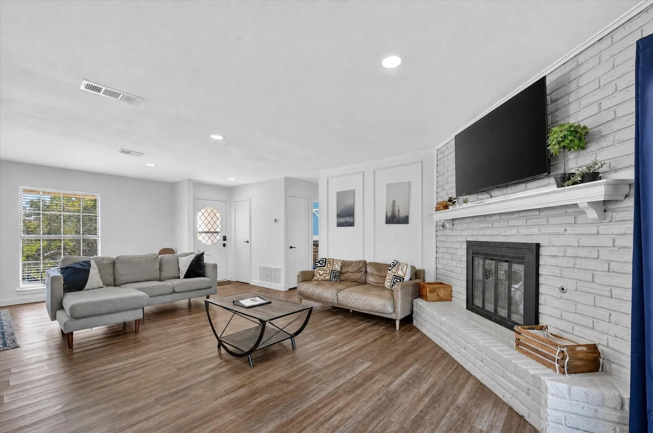 Wood-finish flooring, recessed lighting, and a white brick fireplace with a mantel
