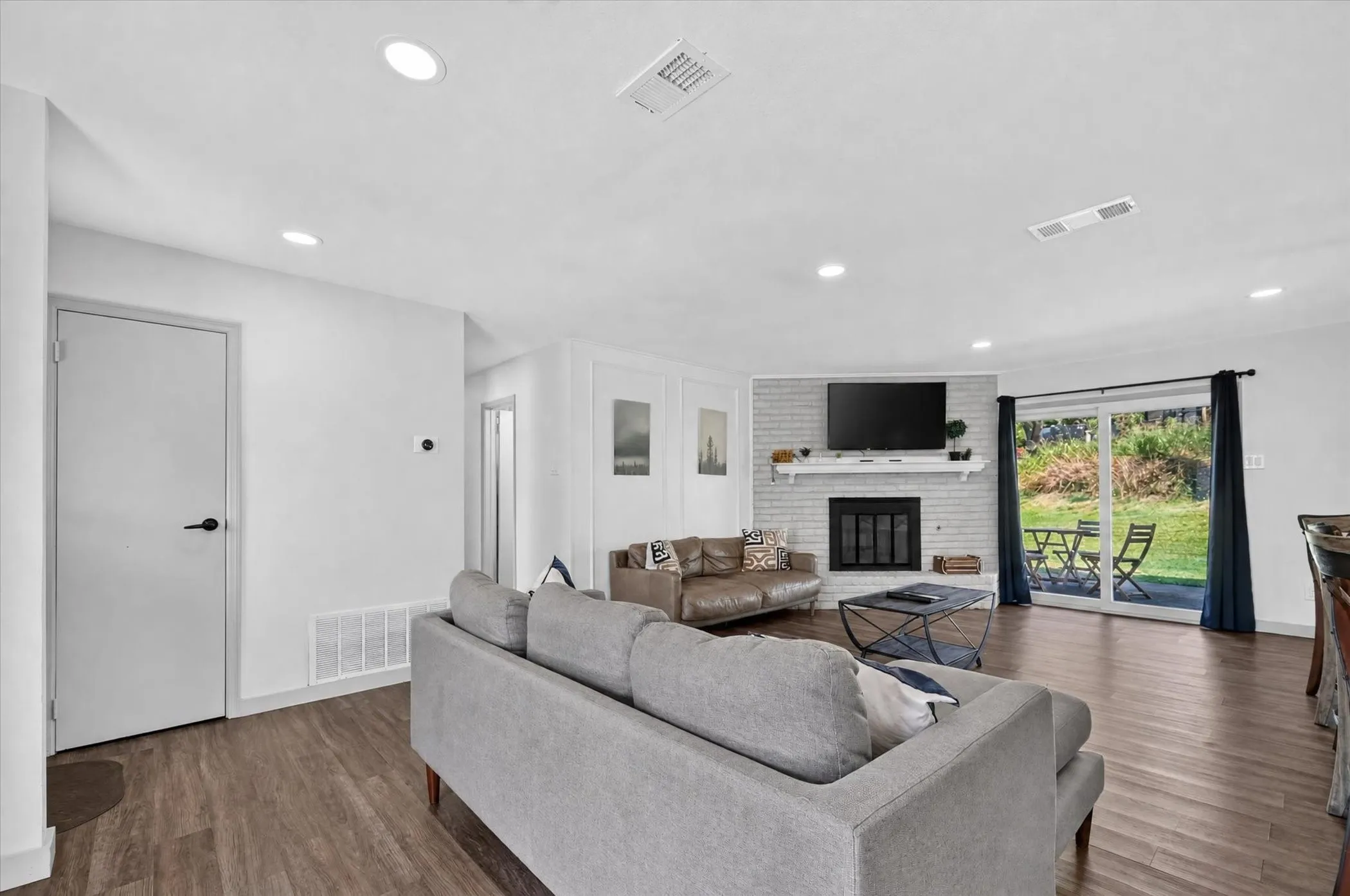 Spacious living area featuring wood-finish flooring, recessed lighting, and a fireplace with a white brick surround and mantel