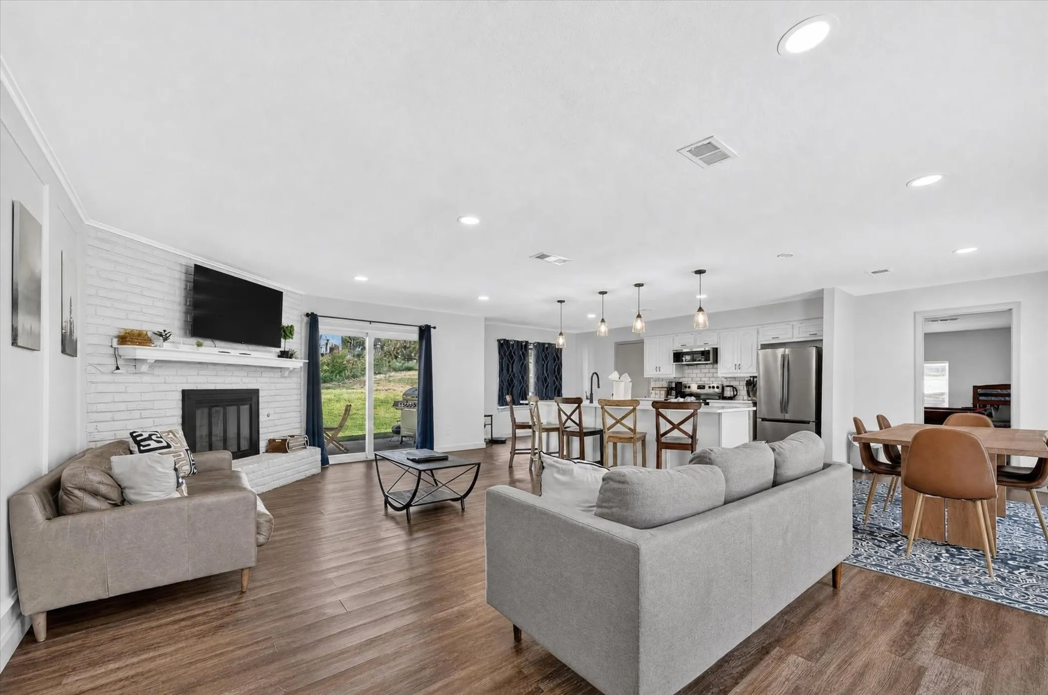 Open-concept living area with wood-finish flooring, a white brick fireplace, and recessed lighting