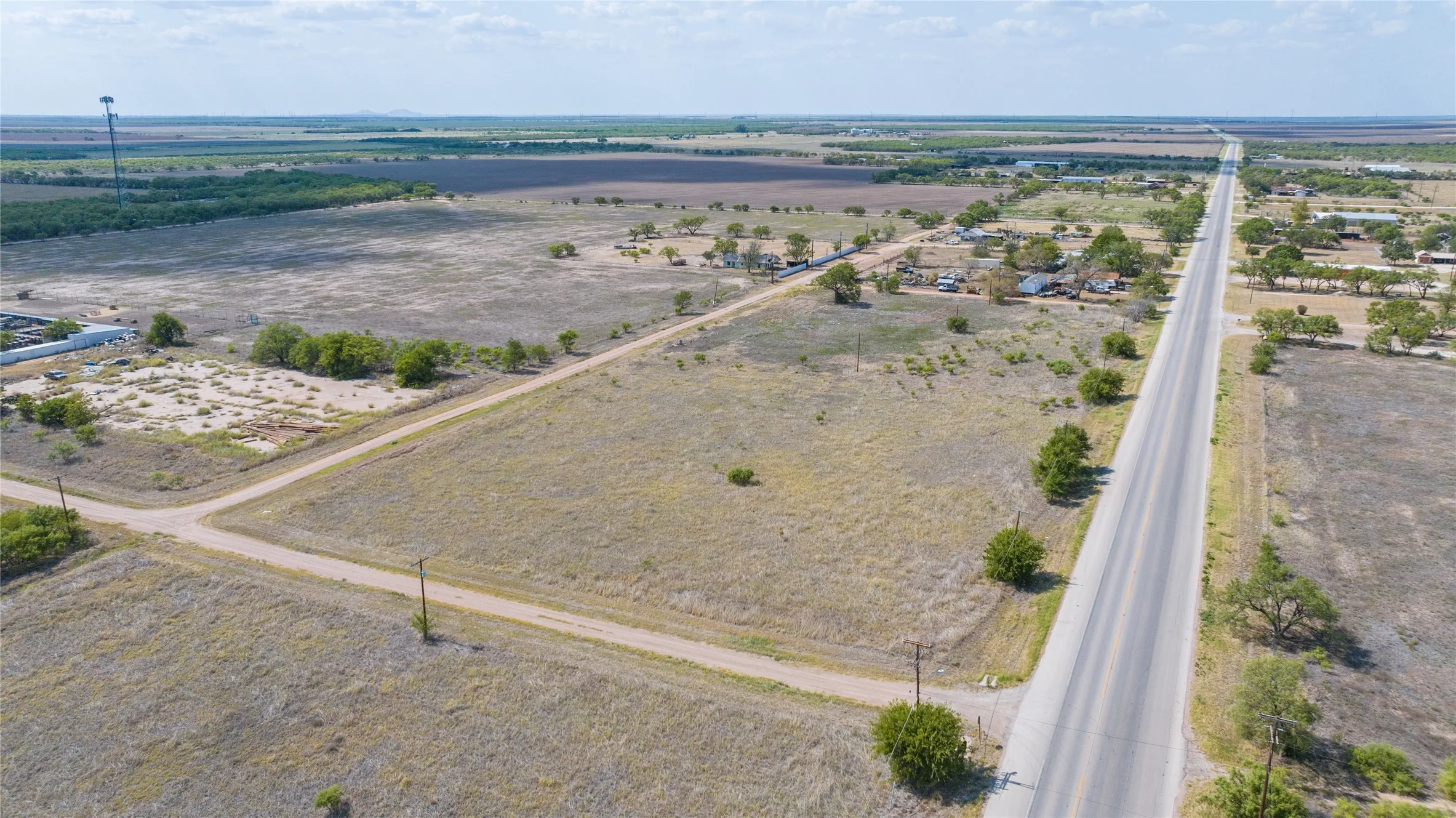Expansive open land with a paved road, scattered mature trees, and a distant treeline