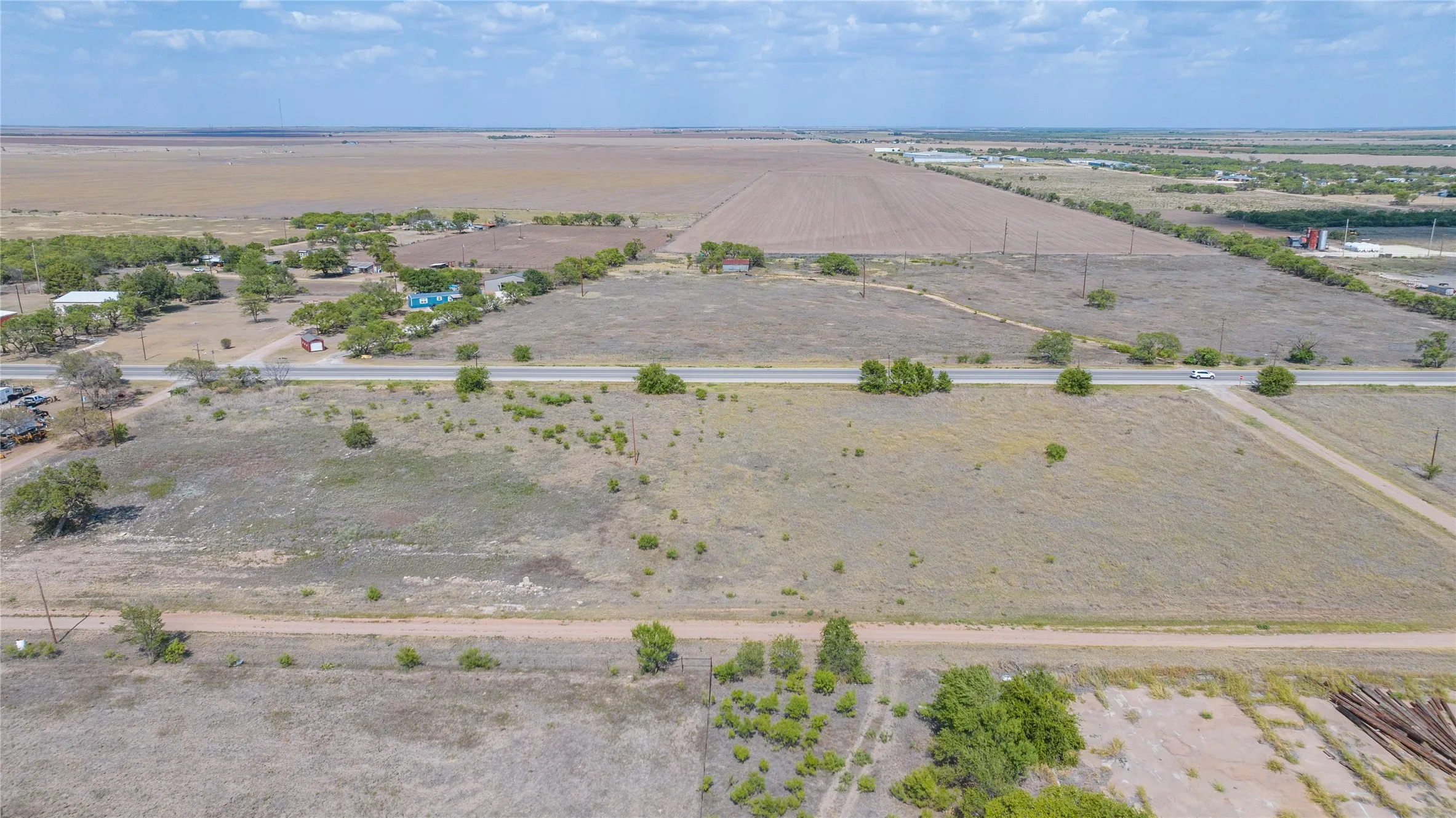Expansive undeveloped land featuring a paved road frontage, established tree lines, and distant agricultural fields