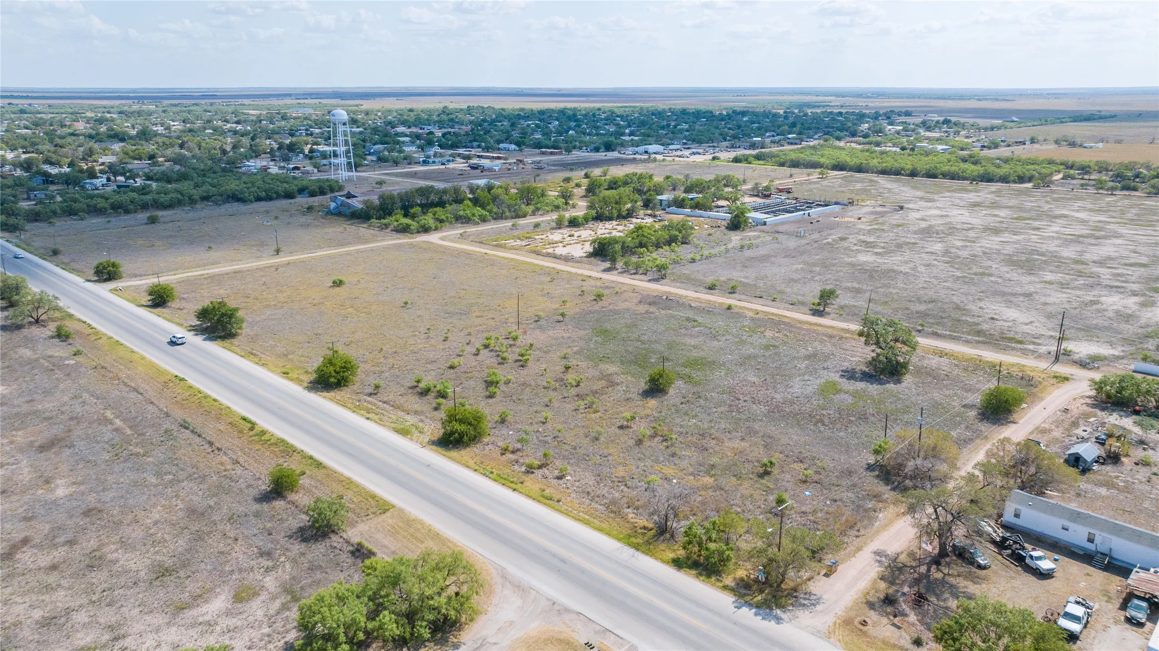 Expansive rural land featuring a paved road, scattered trees, and distant structures