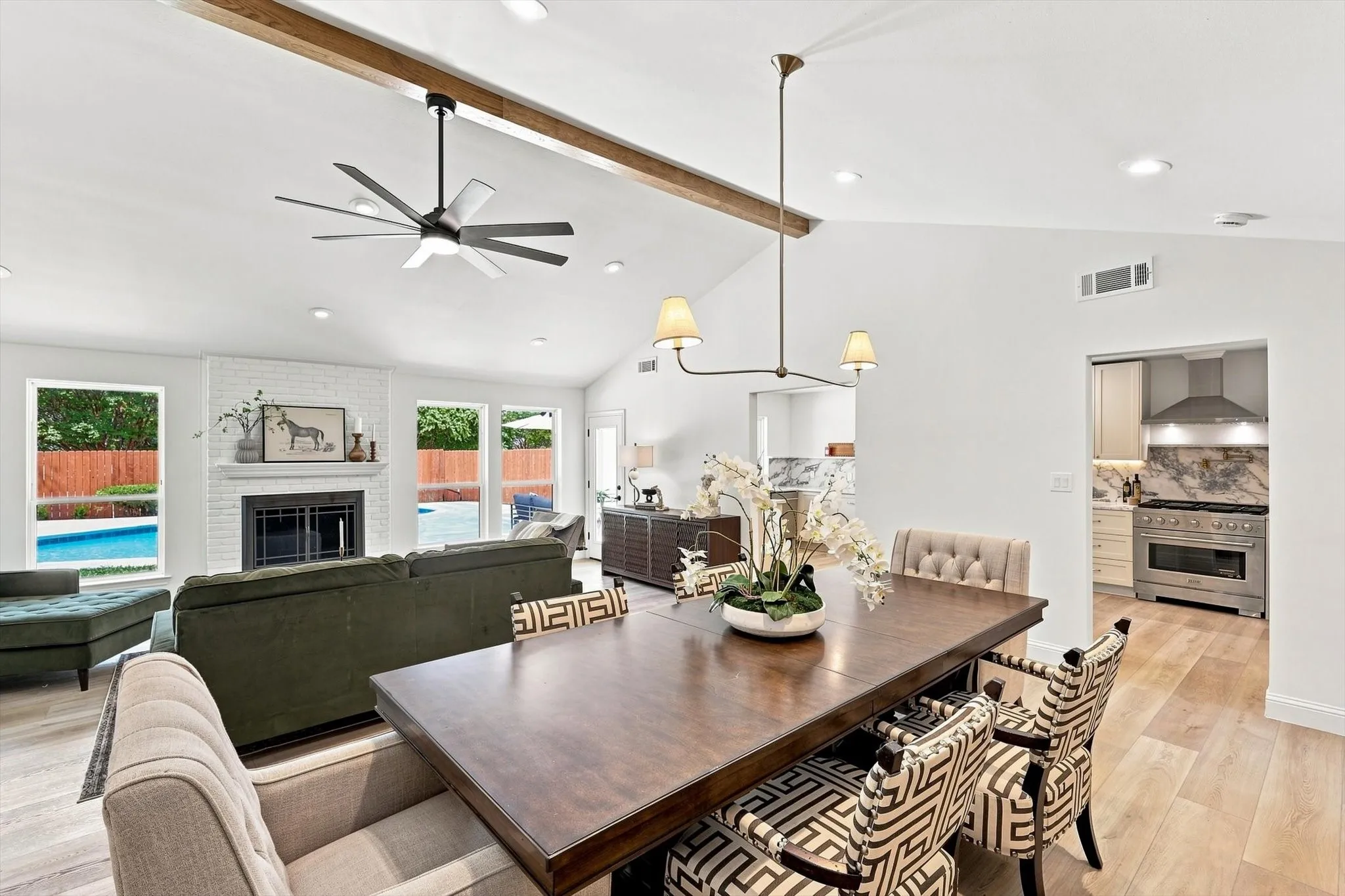 Great view of Dining Room and Living Room featuring contemporary ceiling fan, wood beam, brick fireplace all overlooking backyard space featuring pool.