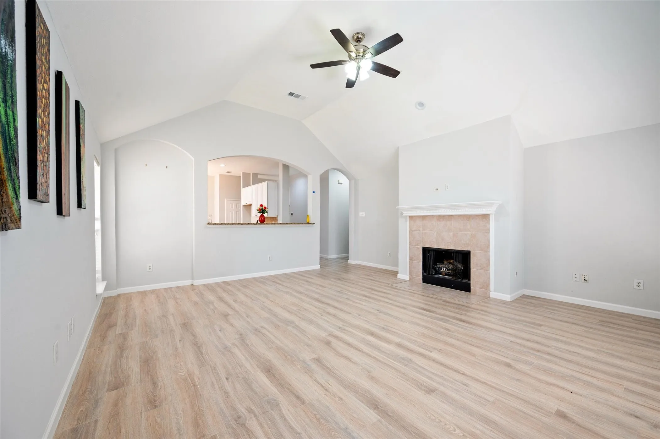 Vaulted ceiling, ceiling fan, wood-finish flooring, fireplace with mantel, and arched pass-through to​​‌​​​​‌​​‌‌​‌‌​​​‌‌​‌​‌​‌​​​‌​​ kitchen