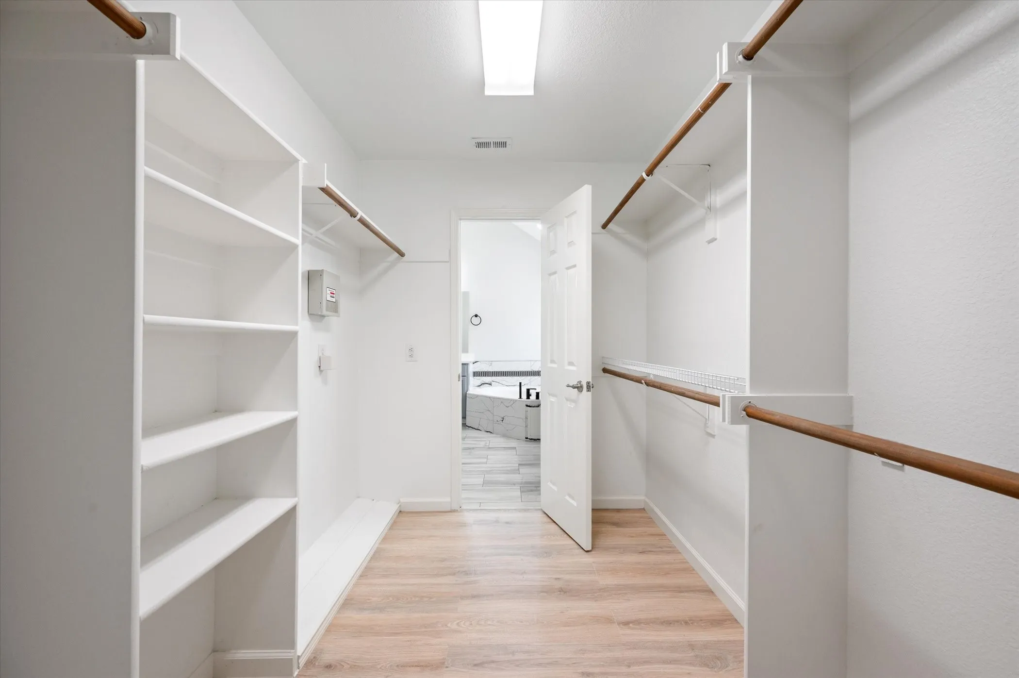 Walk-in closet with wood-finish flooring, built-in shelving, and multiple hanging rods