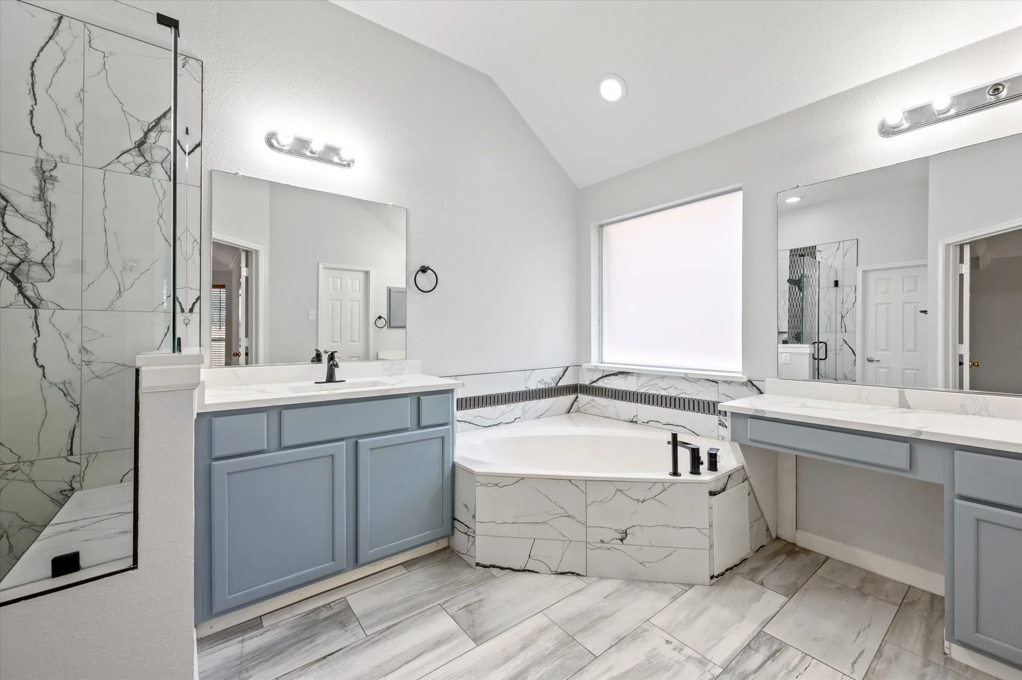 Spacious bathroom with vaulted ceilings, dual vanities, a separate soaking tub, a walk-in shower with glass enclosure, and wood-finish tile flooring