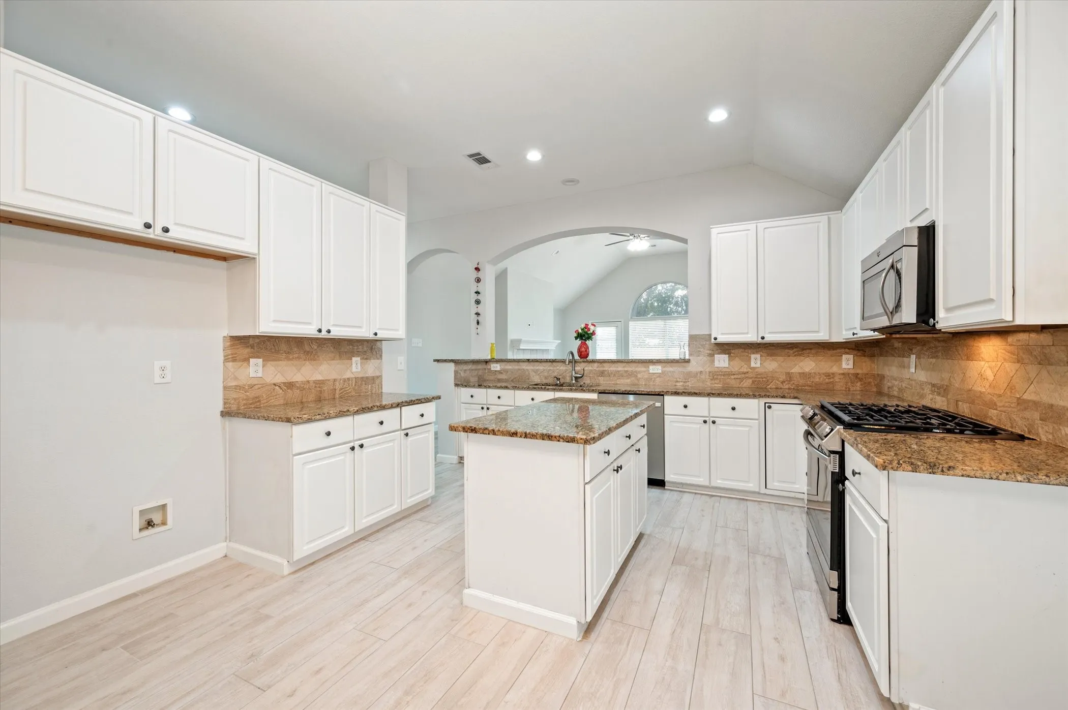 White cabinetry with dark hardware, granite countertops, tile backsplash, stainless steel appliances, and wood-finish flooring