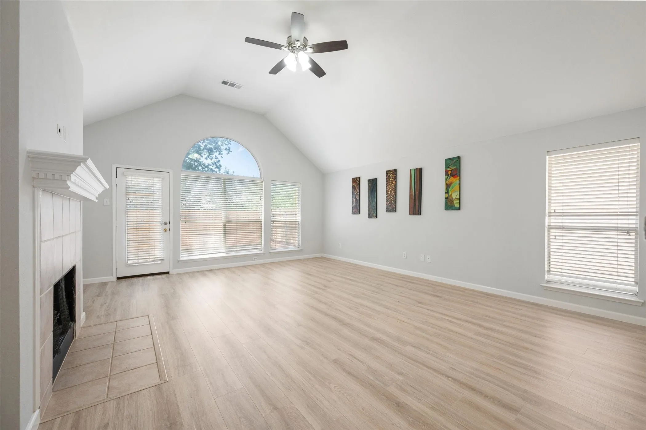 Vaulted ceiling with a ceiling fan, wood-finish flooring, tiled fireplace with mantel, French door, and arched window