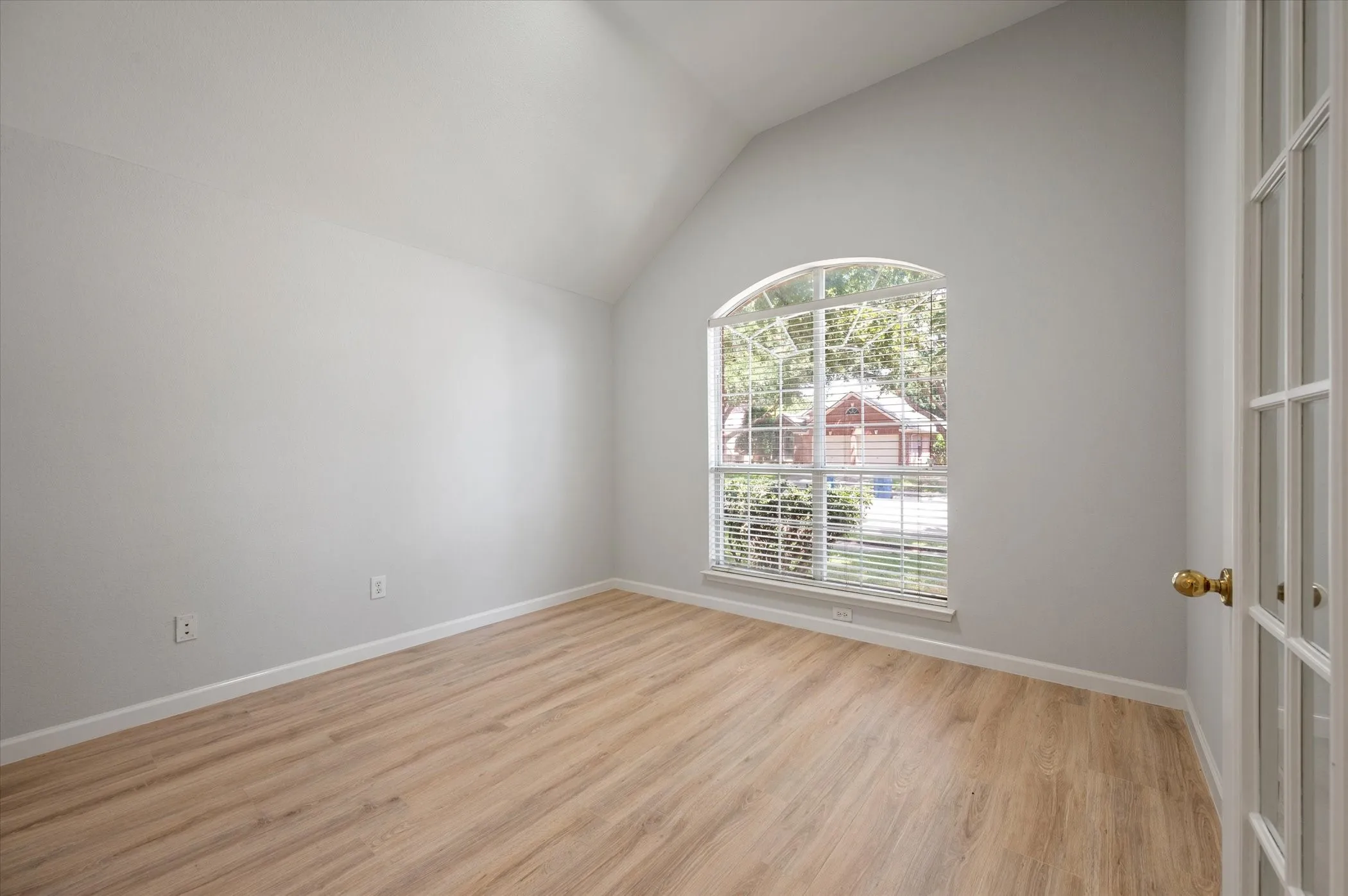 Vaulted ceiling, arched window, wood-finish flooring, white walls, and French door entry