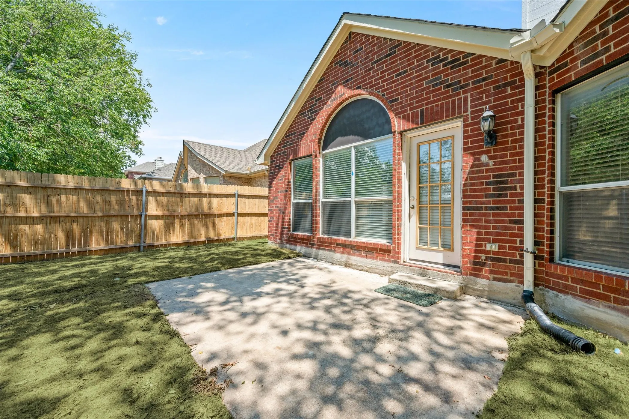 Brick exterior with an arched window, a glass-paneled door, and a concrete patio