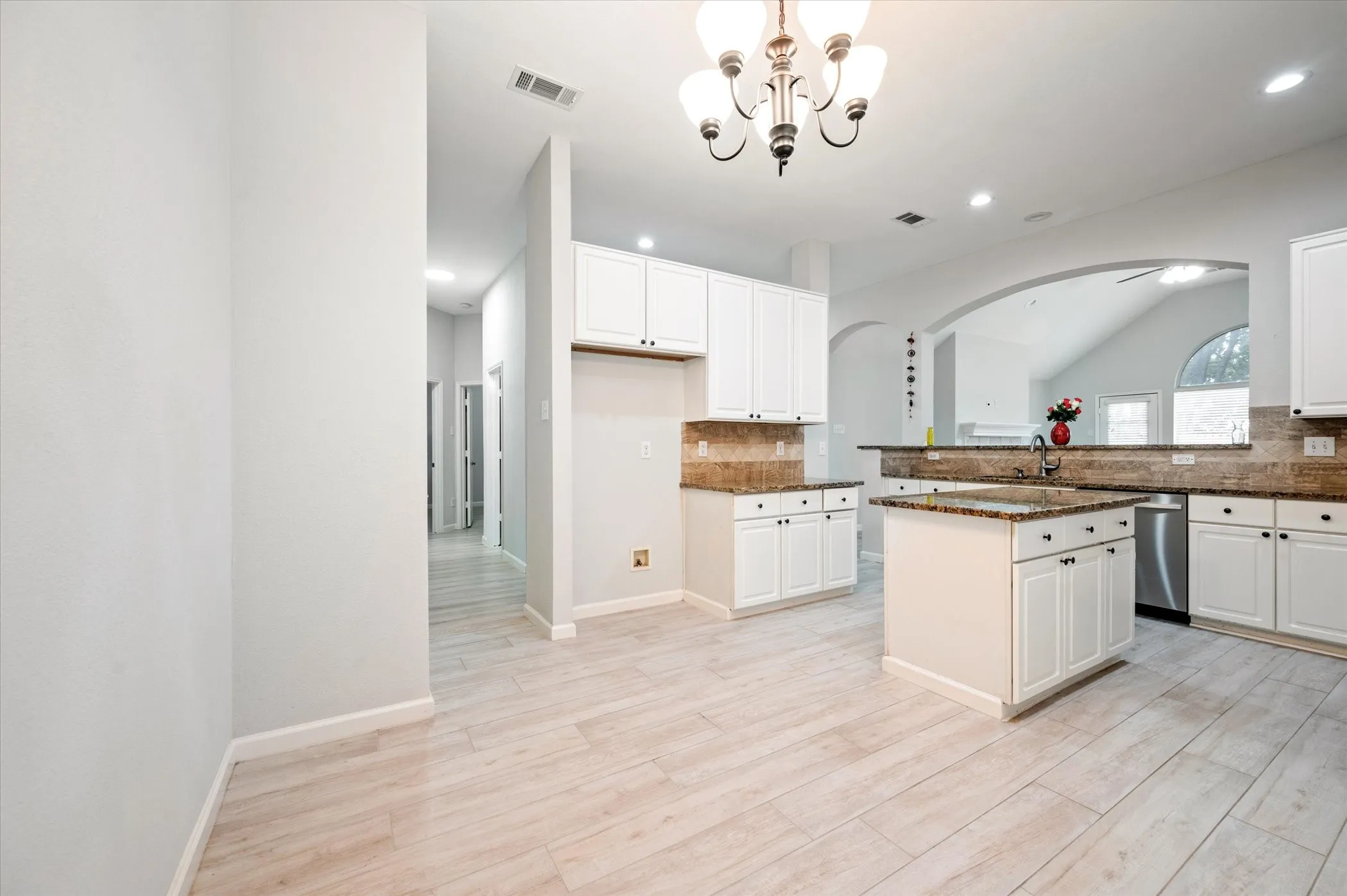 Modern kitchen with light-finish flooring, white cabinetry, dark countertops, and a central island