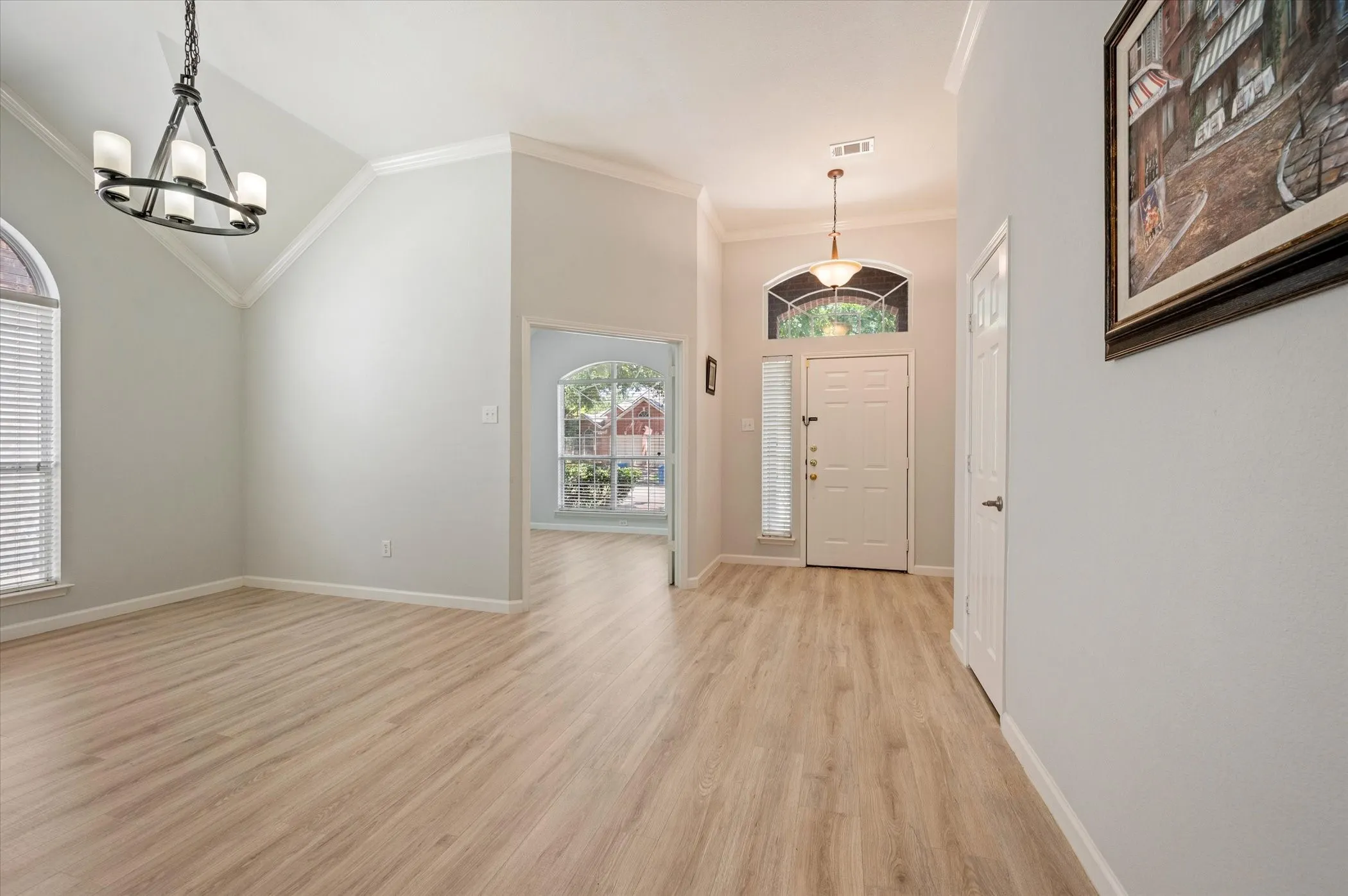 Vaulted ceiling with an iron chandelier, wood-finish flooring, arched window, and a paneled entry door with an arched transom