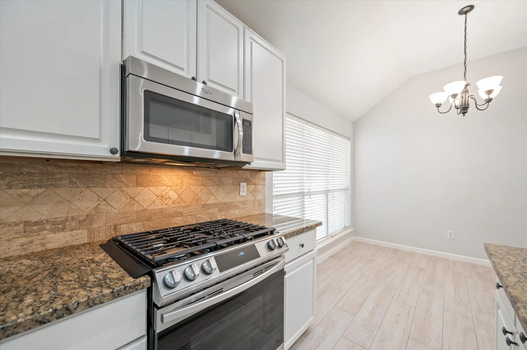 White cabinetry with stainless steel appliances, stone-finish countertops, and a tiled backsplash