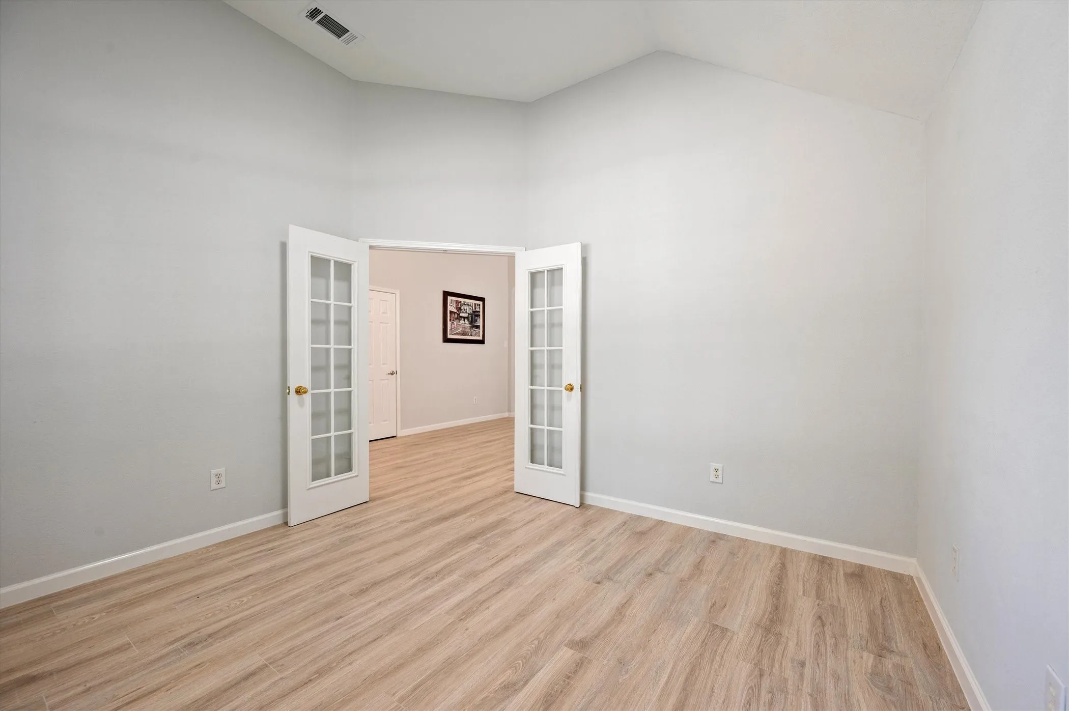 Vaulted ceilings, wood-finish flooring, and double French doors with glass panels