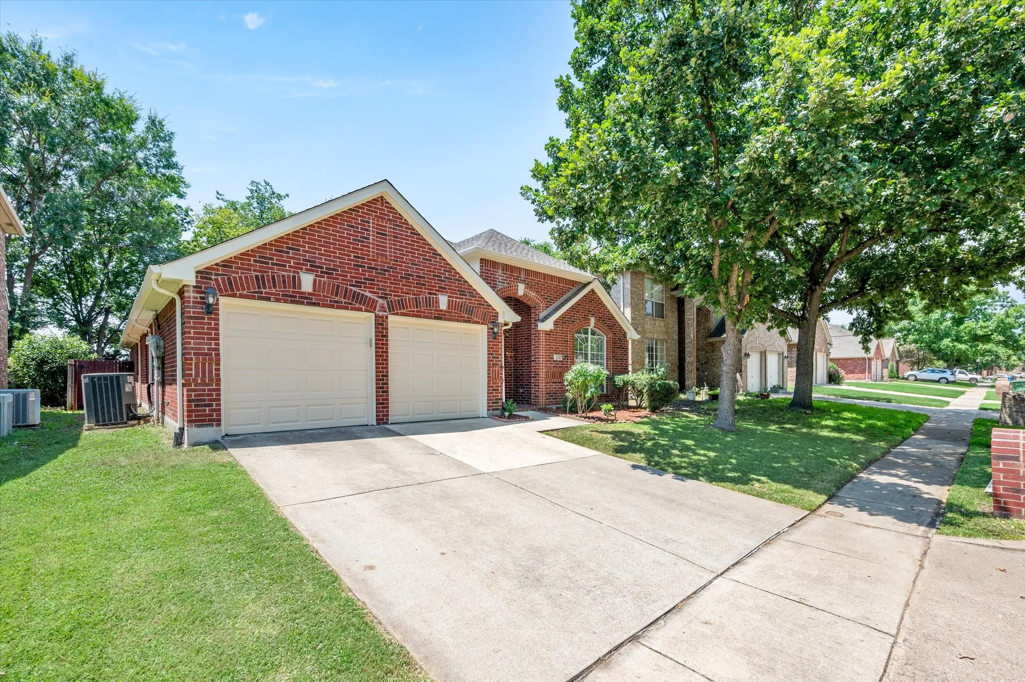 Brick exterior with a gabled roofline, two-car garage, concrete driveway, and mature landscaping