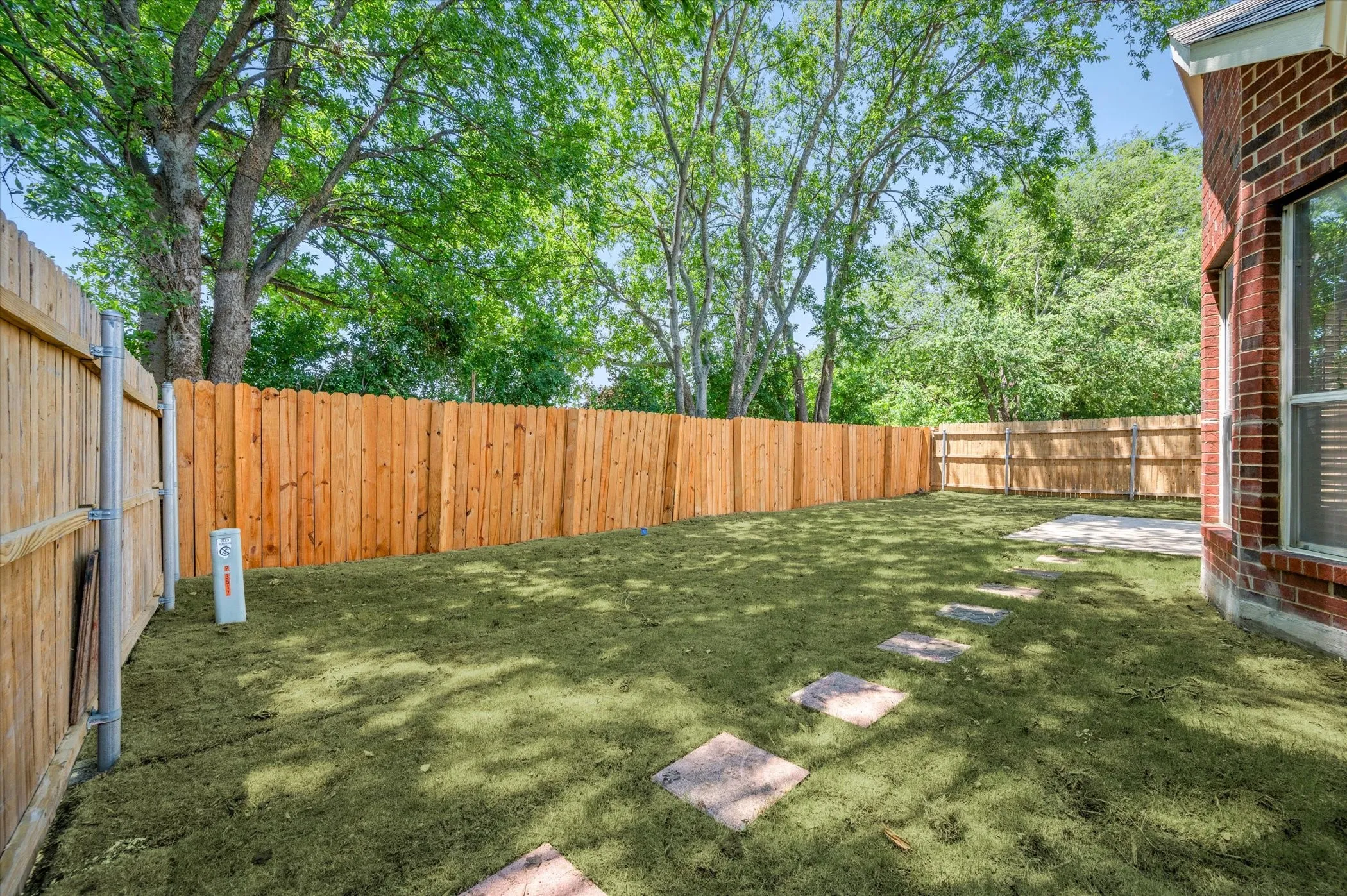 Fenced backyard with a manicured lawn, stone pathway, and mature trees