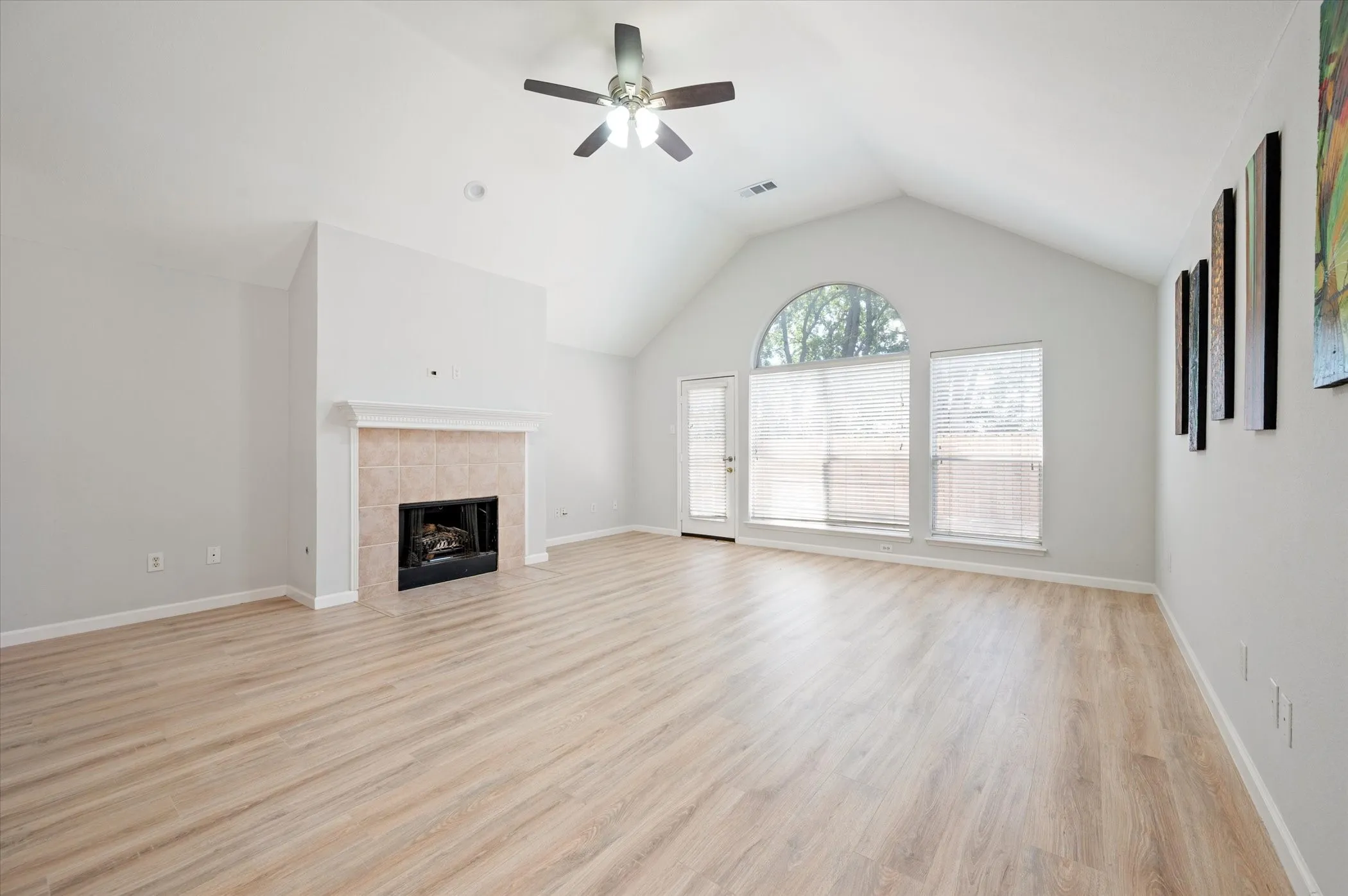Spacious interior featuring wood-finish flooring, vaulted ceilings, a fireplace with a tiled surround, and an arched transom window