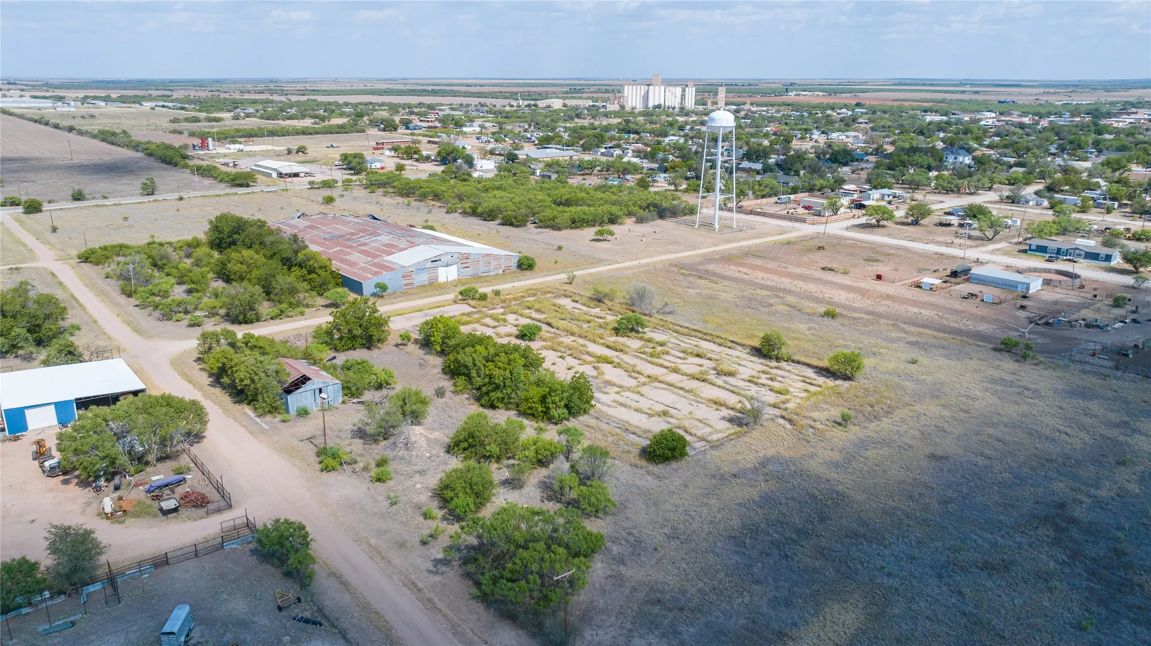 Expansive land parcel featuring multiple outbuildings, including a large corrugated metal structure and a blue and white barn
