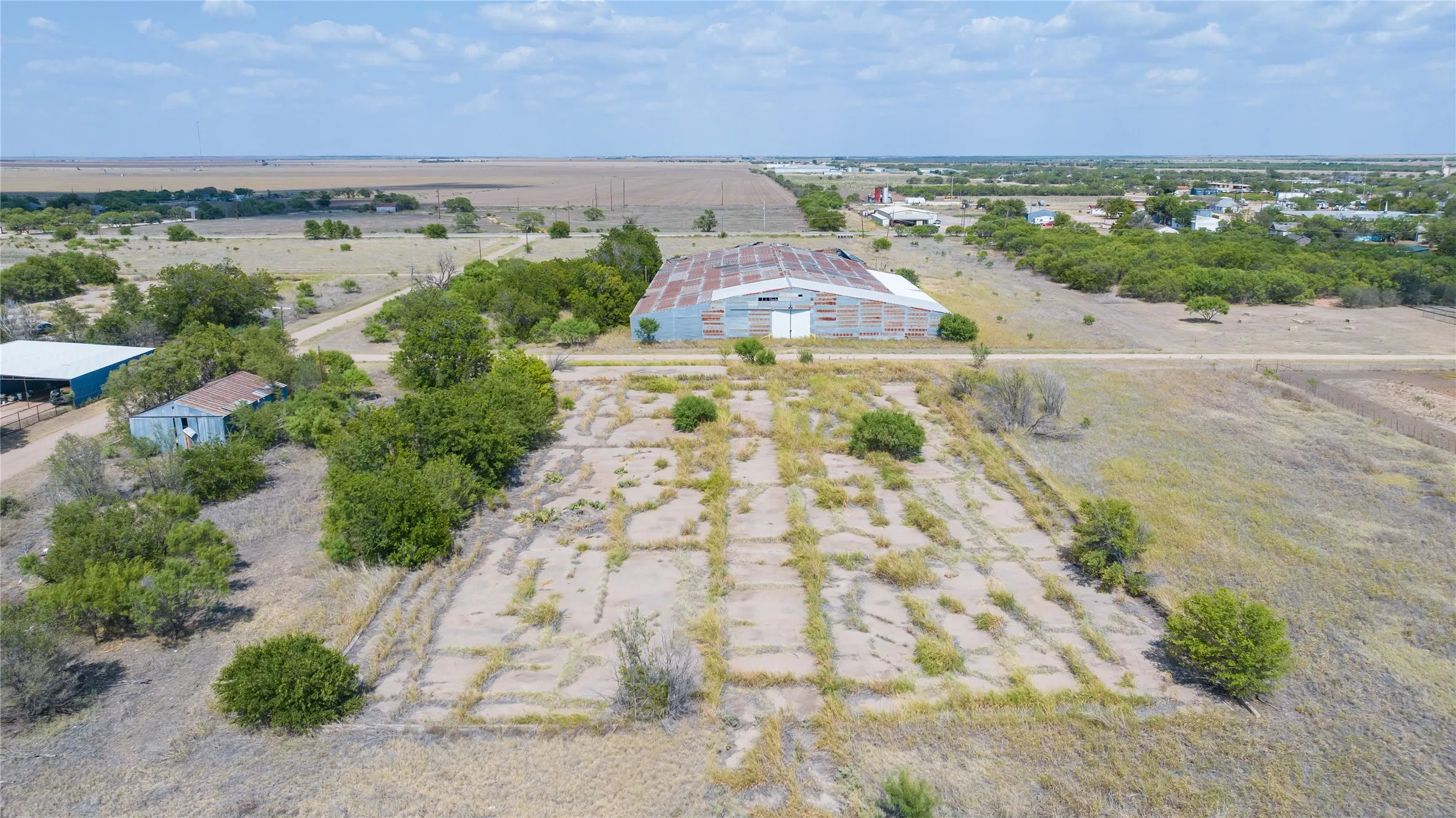Expansive rural property featuring a large metal-sided outbuilding with a corrugated roof, additional smaller structures, and established trees