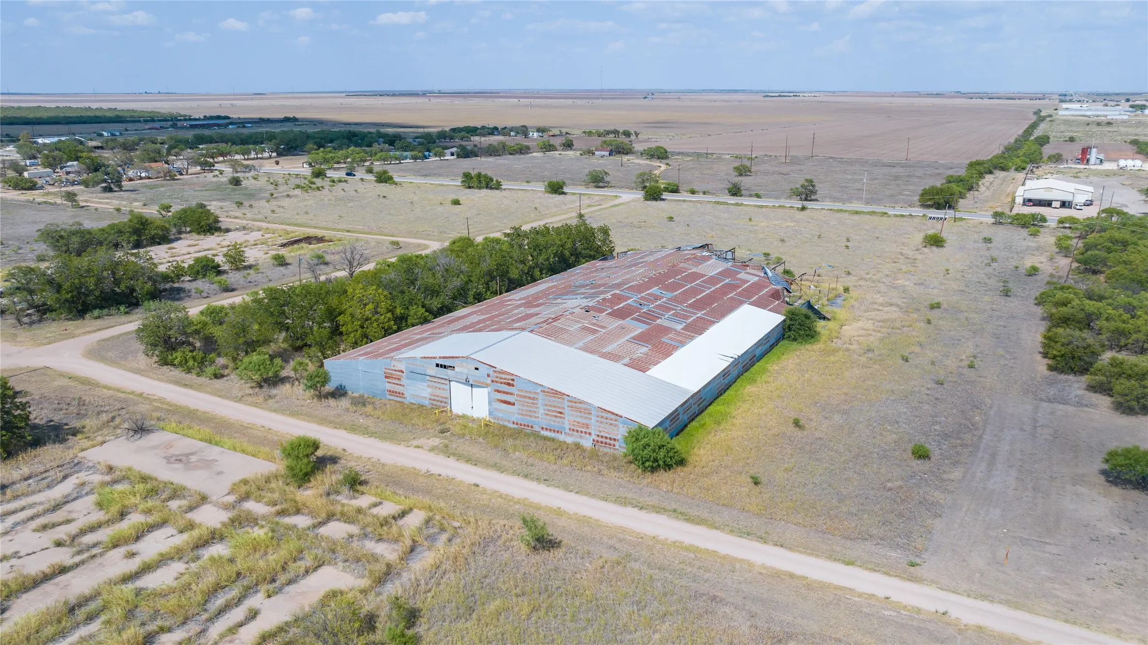 Large industrial building with a corrugated metal roof and siding, situated on a substantial land parcel with a dirt road access point