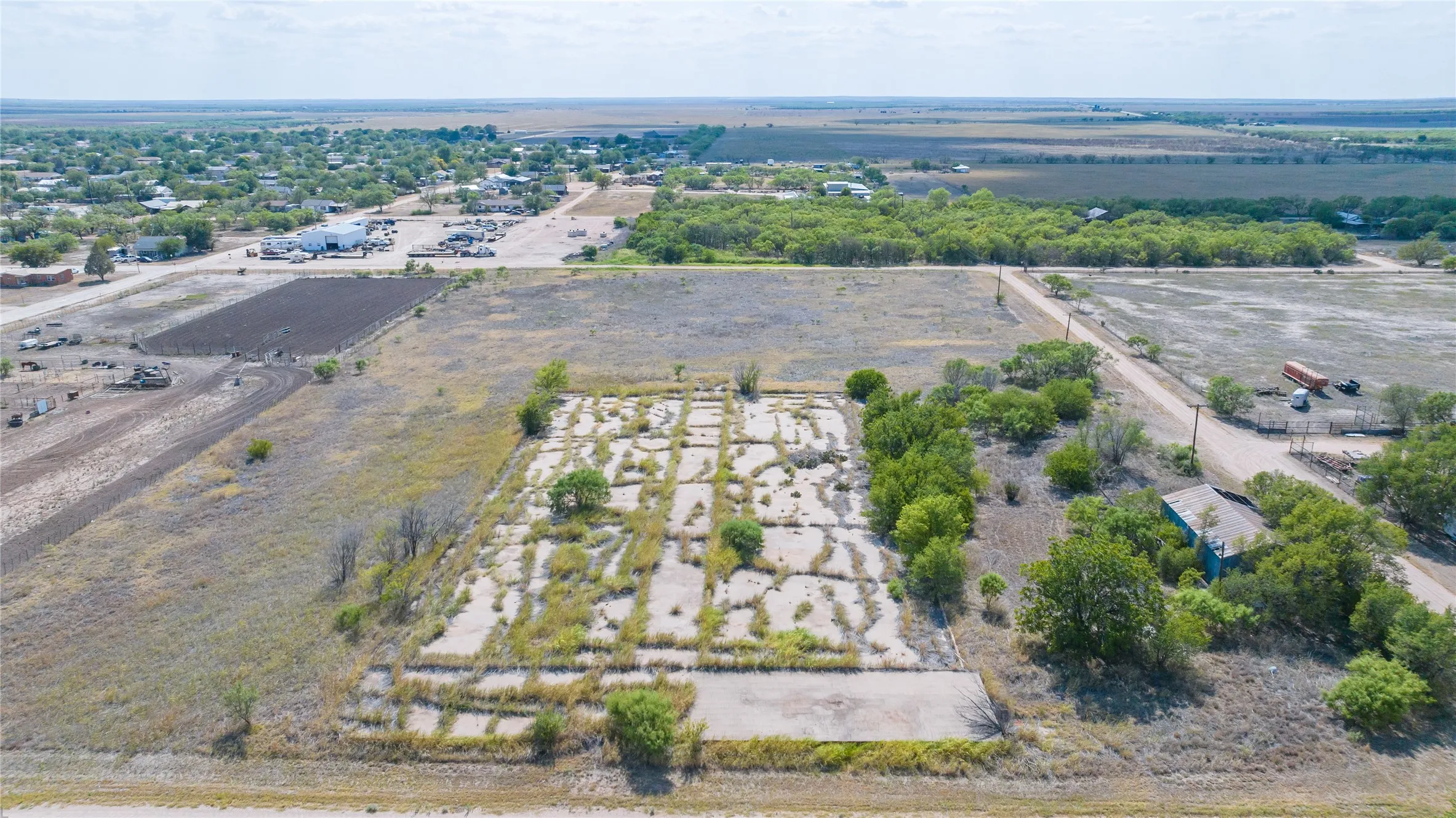 Expansive rural land featuring a partial concrete pad and scattered trees
