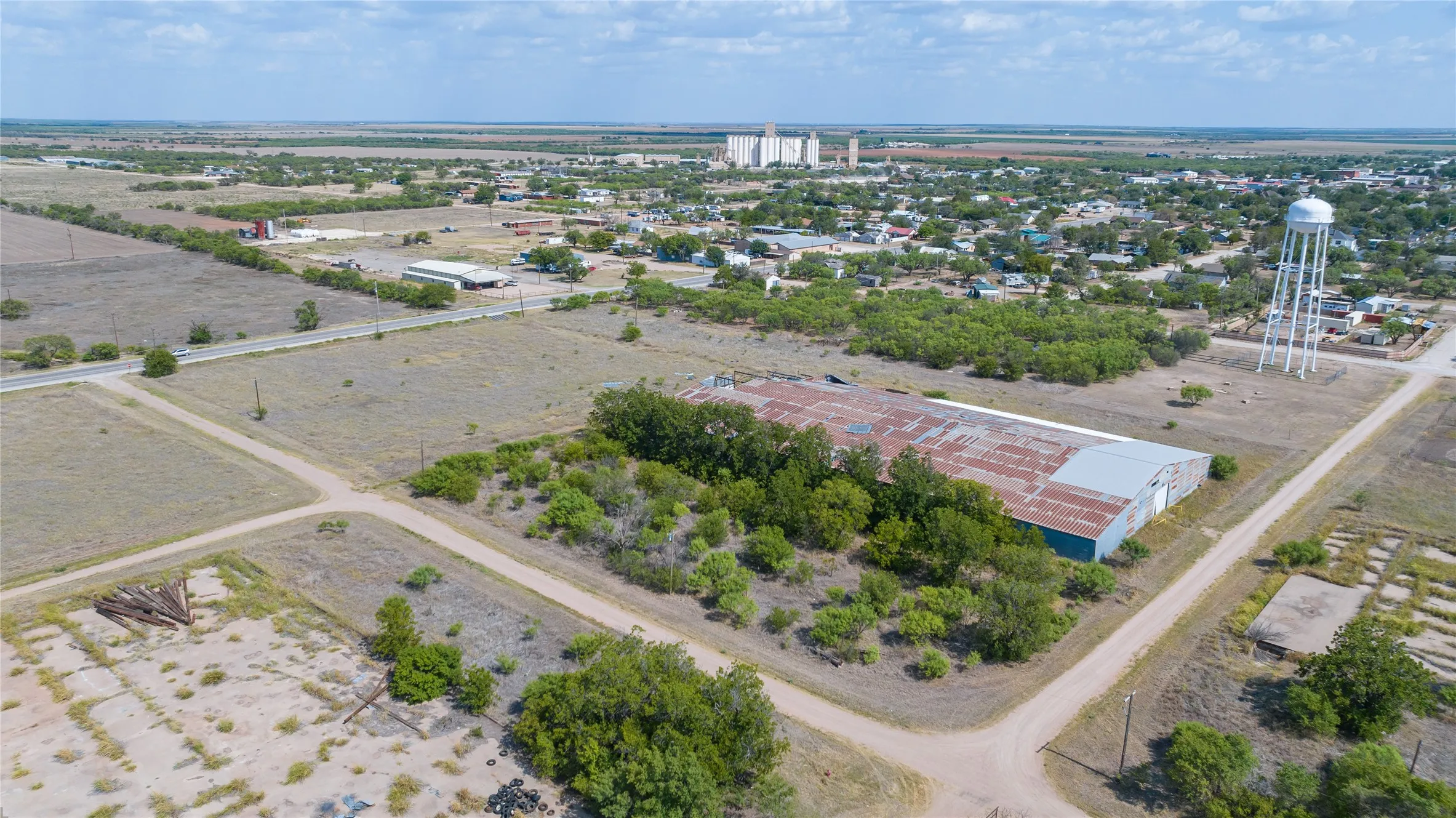 Expansive land parcel featuring an industrial building with a corrugated metal roof, surrounding green spaces, and direct access to a paved road