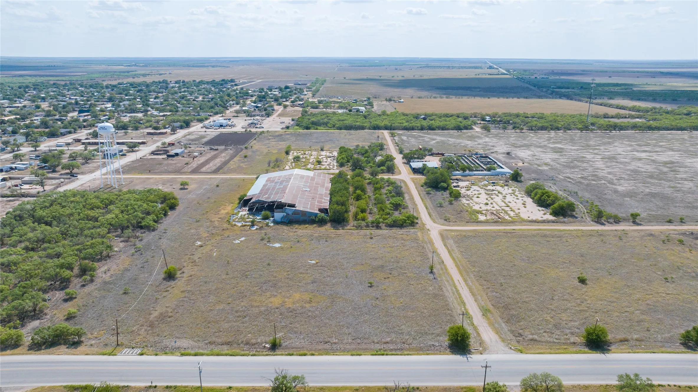 Expansive land parcel featuring a large agricultural building, multiple cleared areas, and direct road frontage