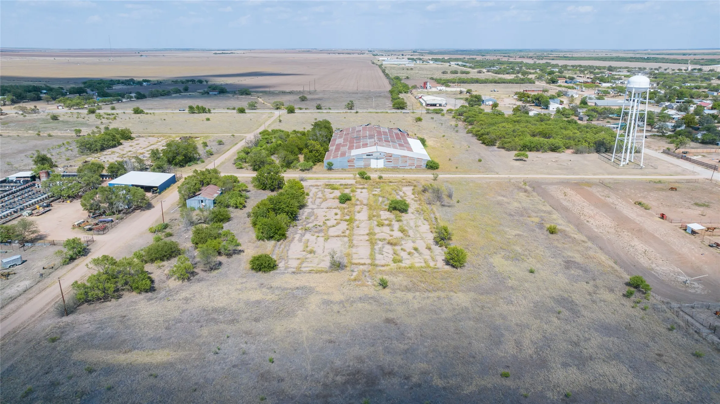 Expansive rural property featuring a large metal-roofed barn, an additional structure with a blue roof, and a water tower in the distance