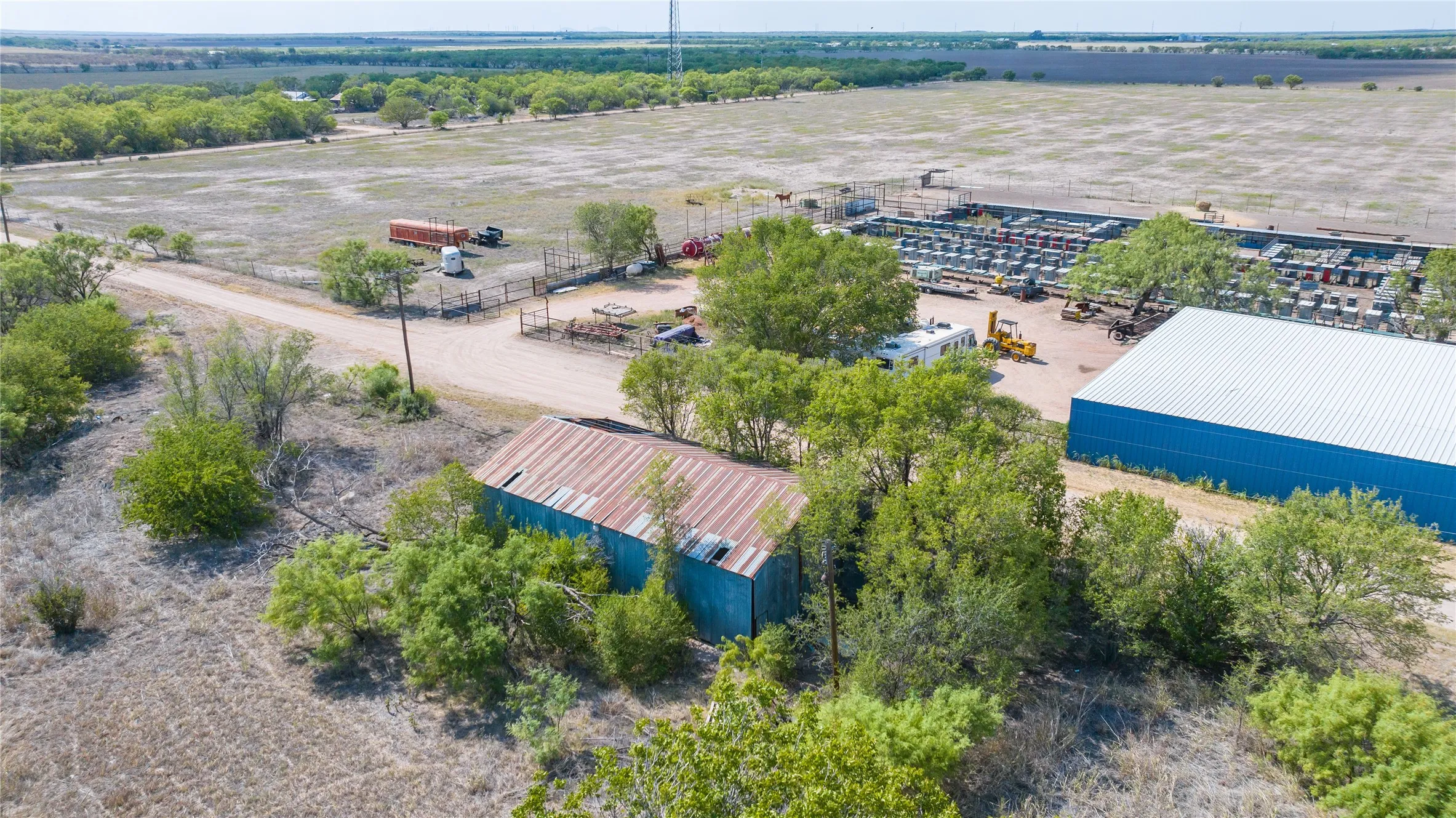 Large blue metal building with a white roof, expansive open fields, and a dirt road