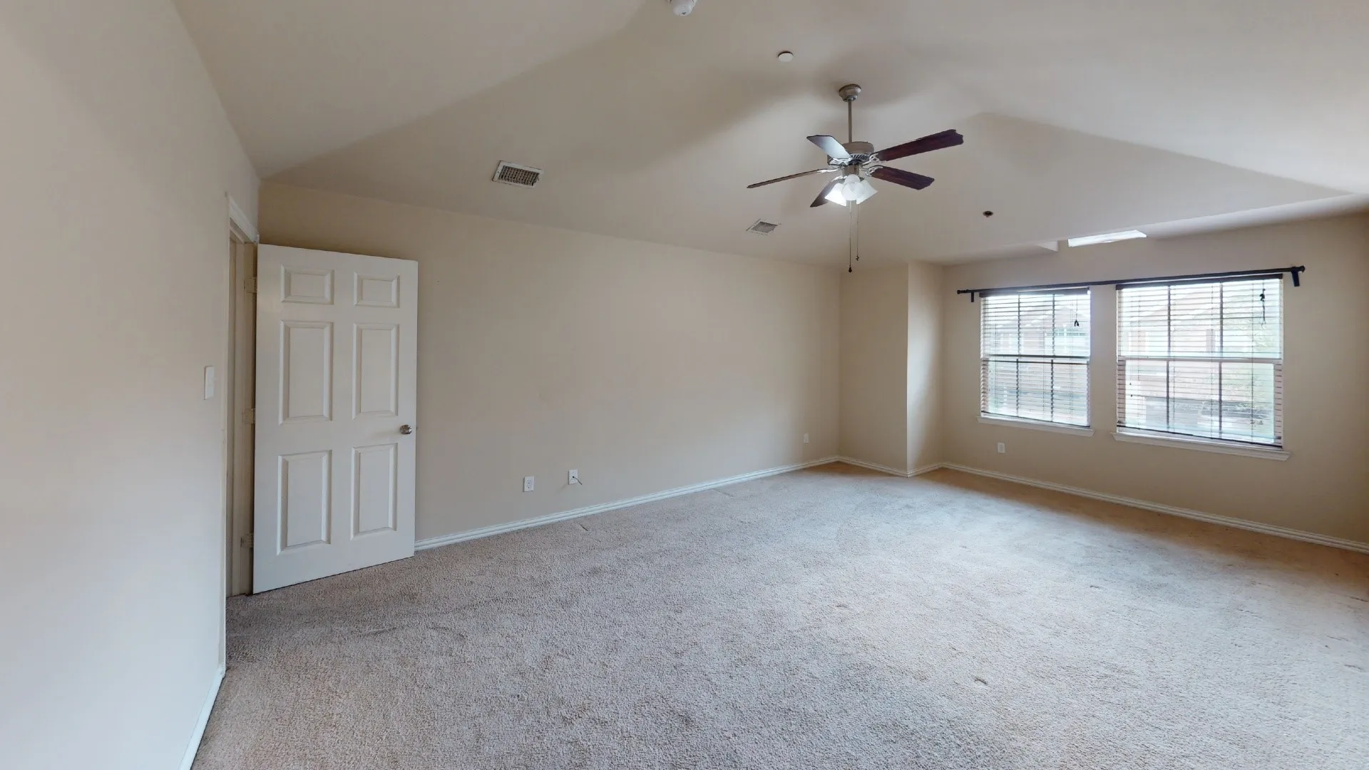 Spacious room featuring vaulted ceilings, carpeted flooring, a ceiling fan, and two windows