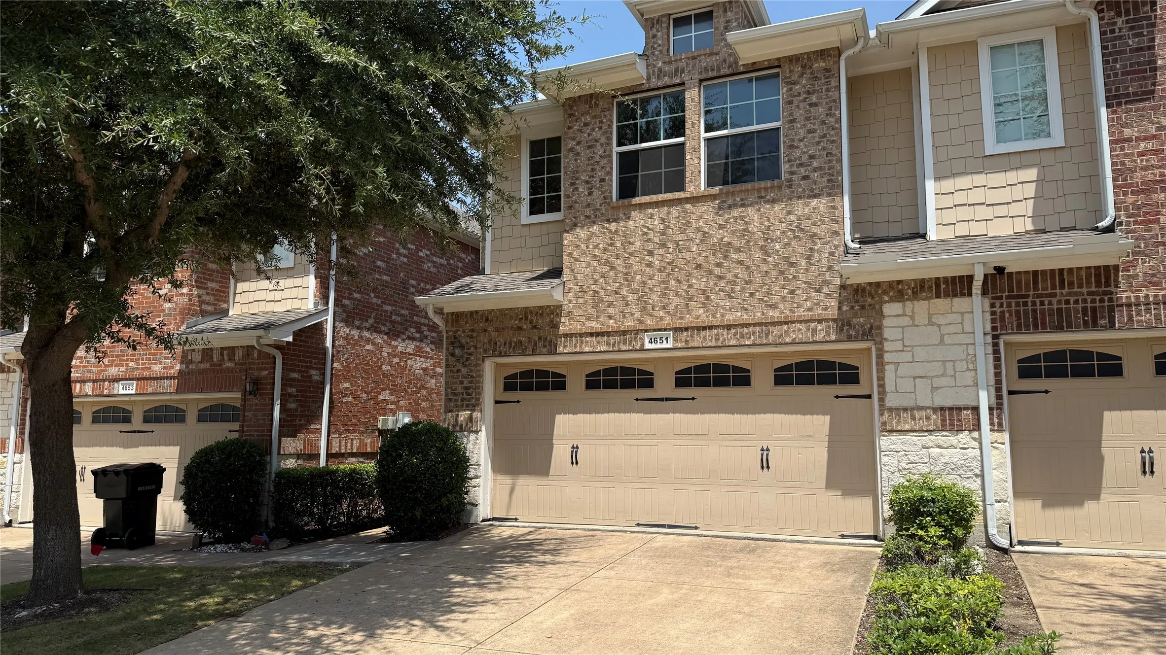 Brick and stone facade with shake siding accents, two-car garage with arched window detailing, and mature landscaping