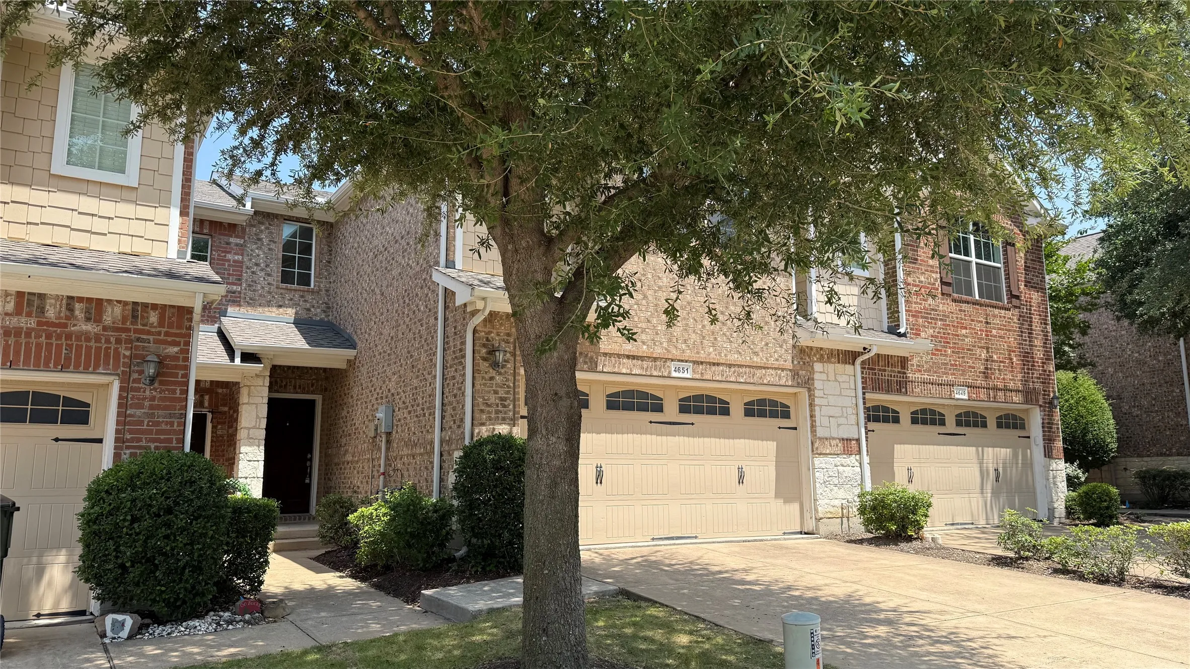 Brick and stone facade with shake siding accents, multiple bay garage doors with arched window details, and mature landscaping