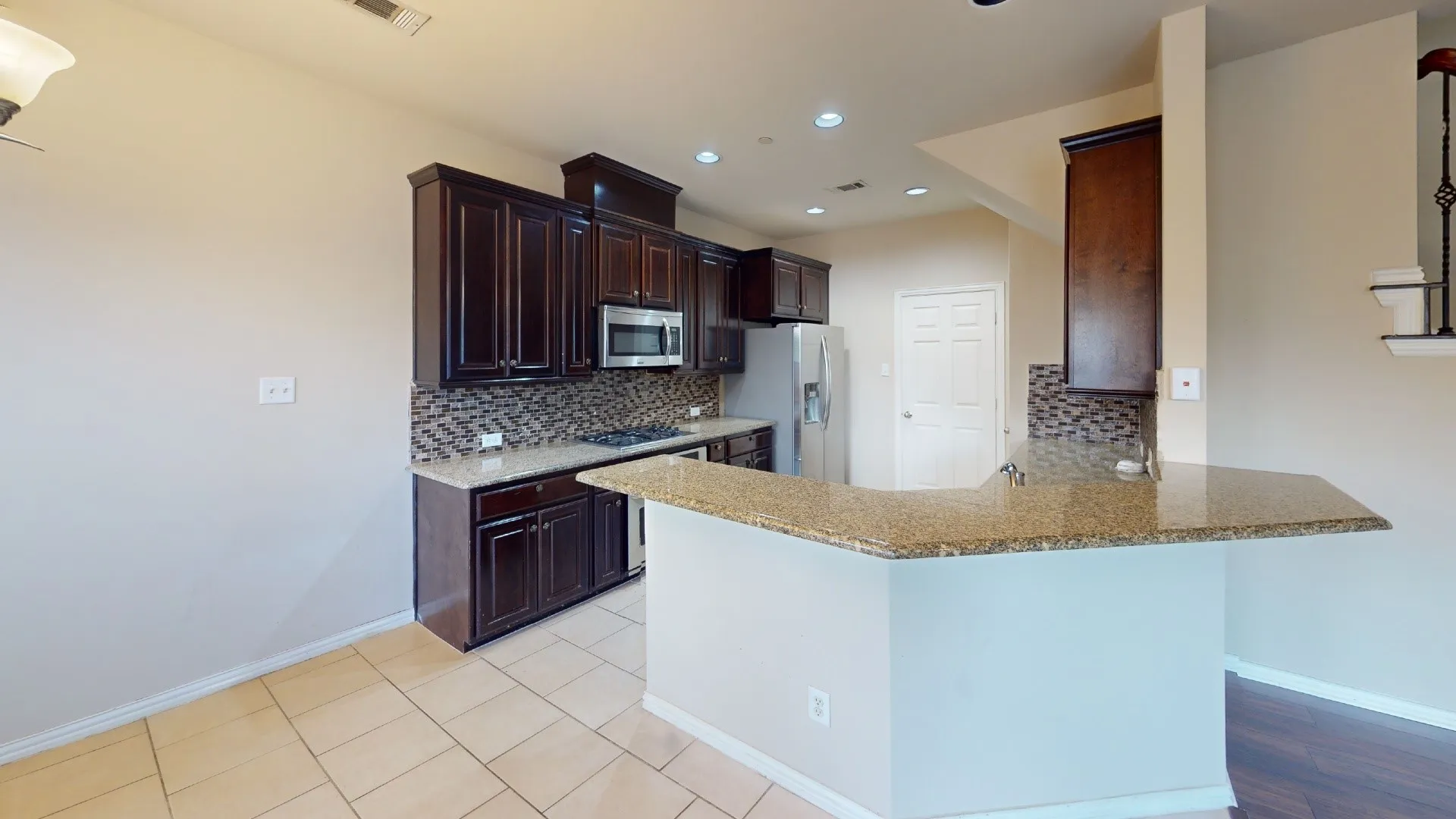 Kitchen featuring dark wood cabinetry, granite countertops, tile backsplash, and stainless steel appliances
