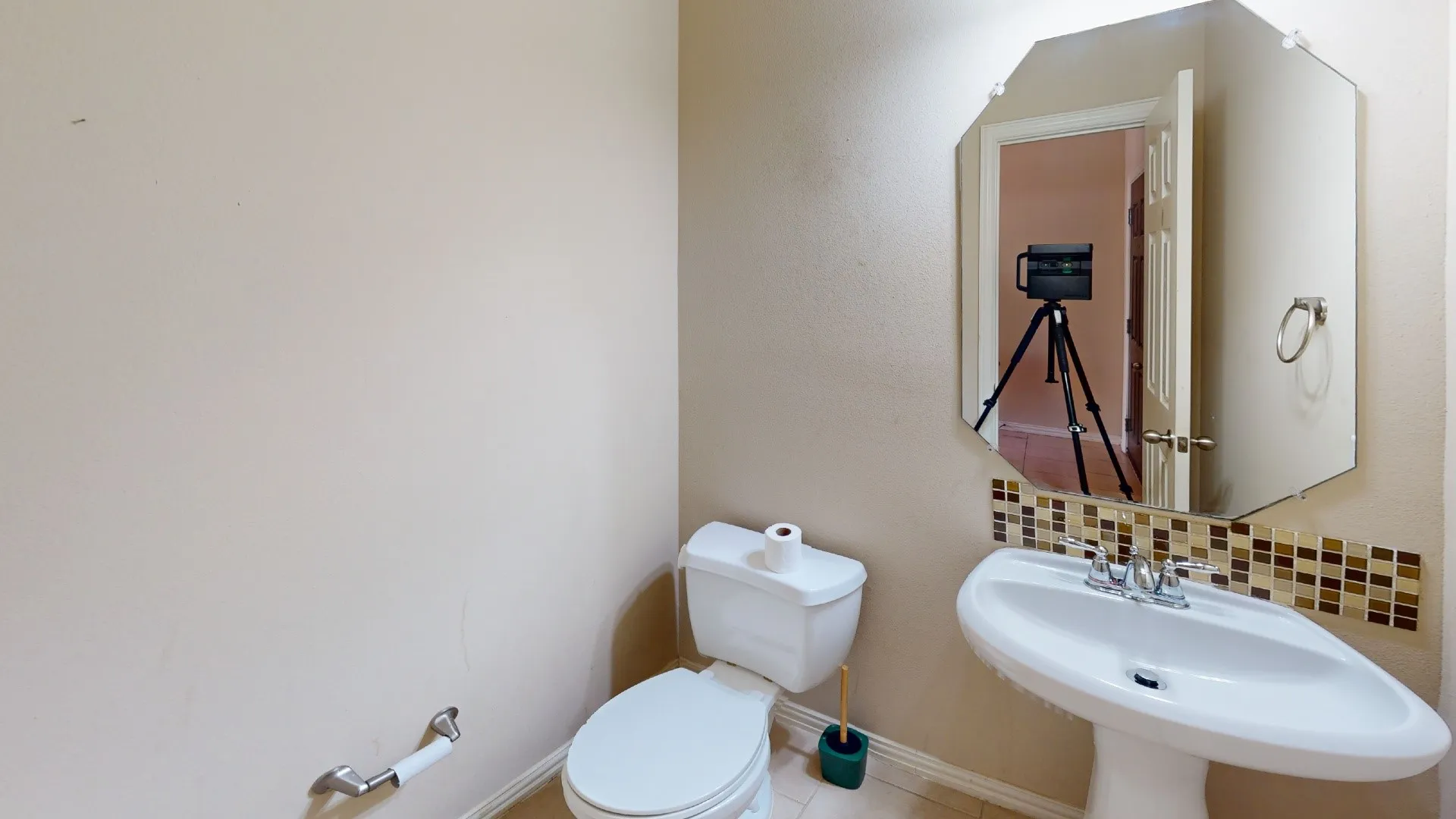 White pedestal sink with a chrome faucet, complemented by a mosaic tile backsplash