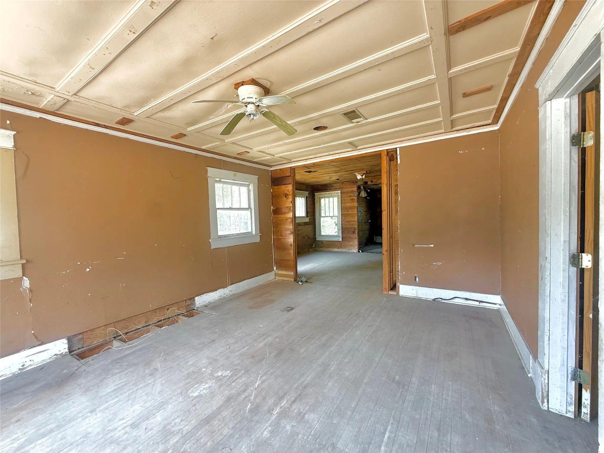 Coffered ceiling detail, ceiling fan with light fixture, multiple windows, exposed wood wall elements, and wood-finish flooring
