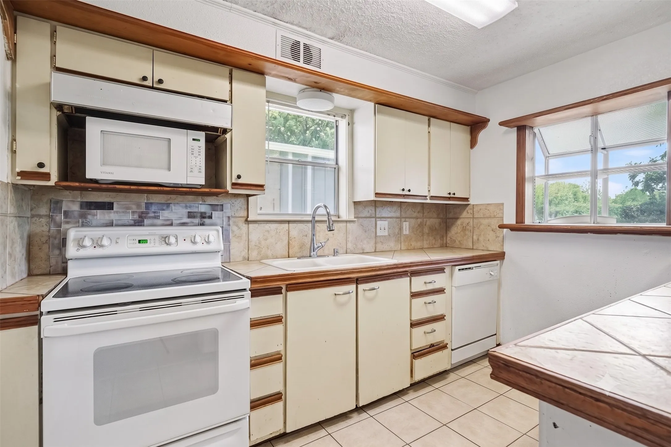 Kitchen cooking area featuring white electric range, built-in microwave, upper storage cabinets, and window.