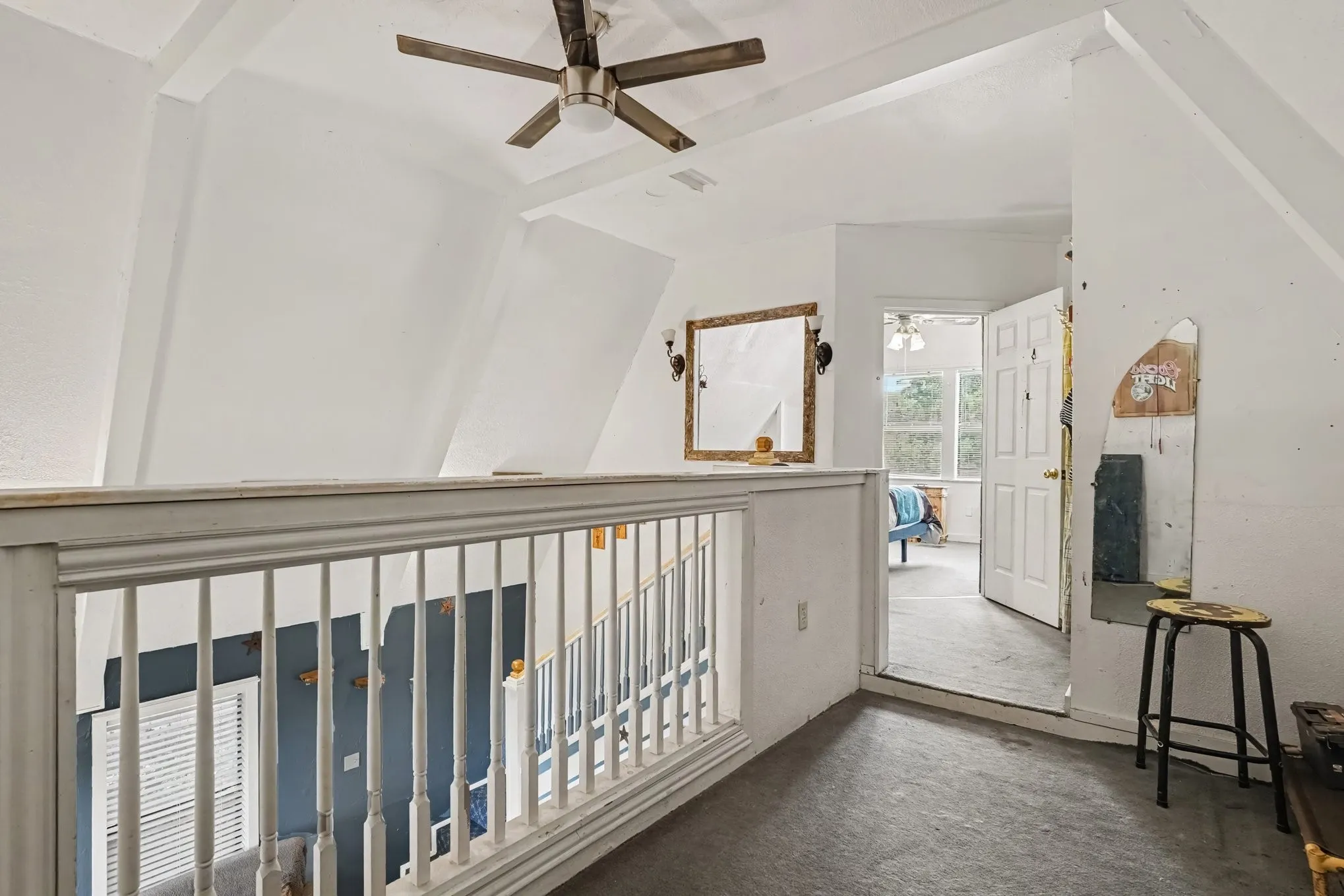 Upper loft landing overlooking the main floor living space, complete with wooden railing and ceiling fan.
