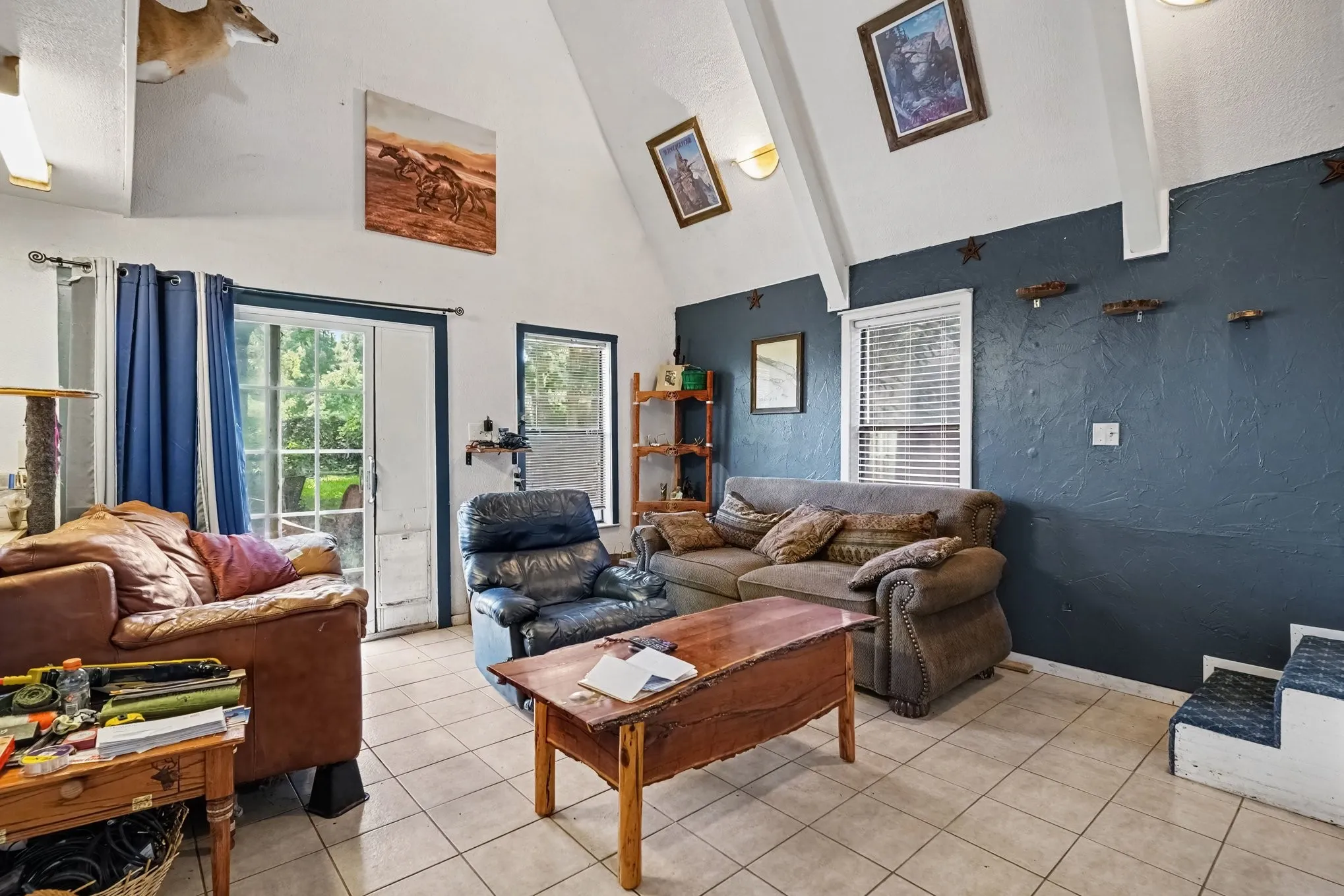Spacious two-story living room featuring soaring vaulted ceilings, dark blue accent walls, tile flooring, and abundant natural light.