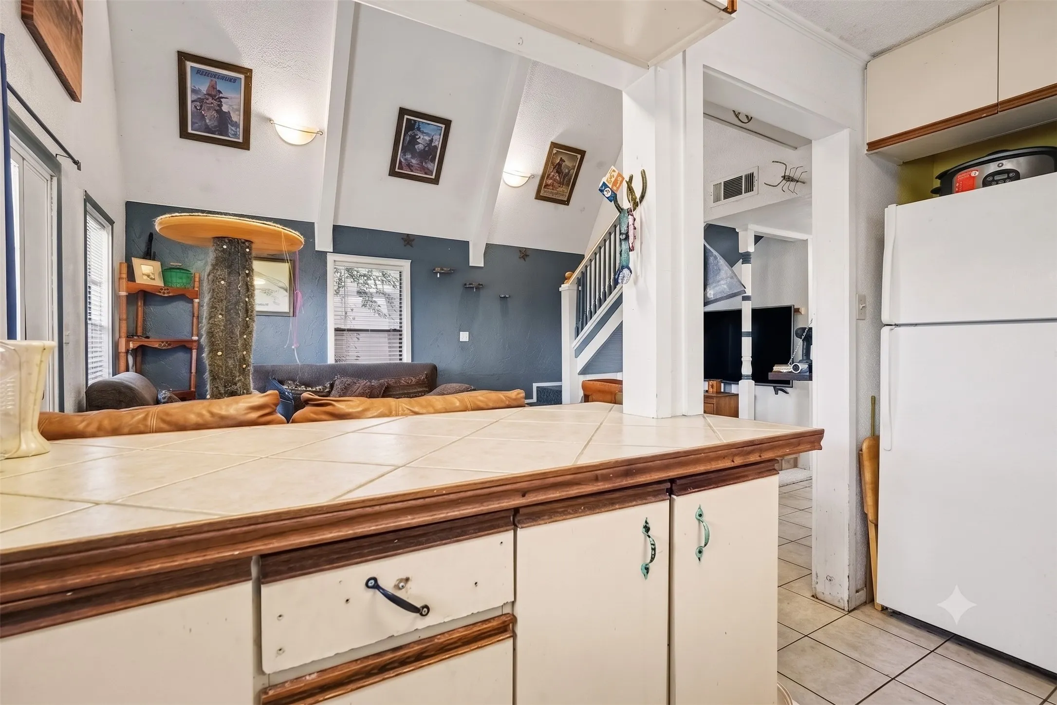 Functional kitchen equipped with dual-tone cabinetry, light countertops, refrigerator, and tile flooring.