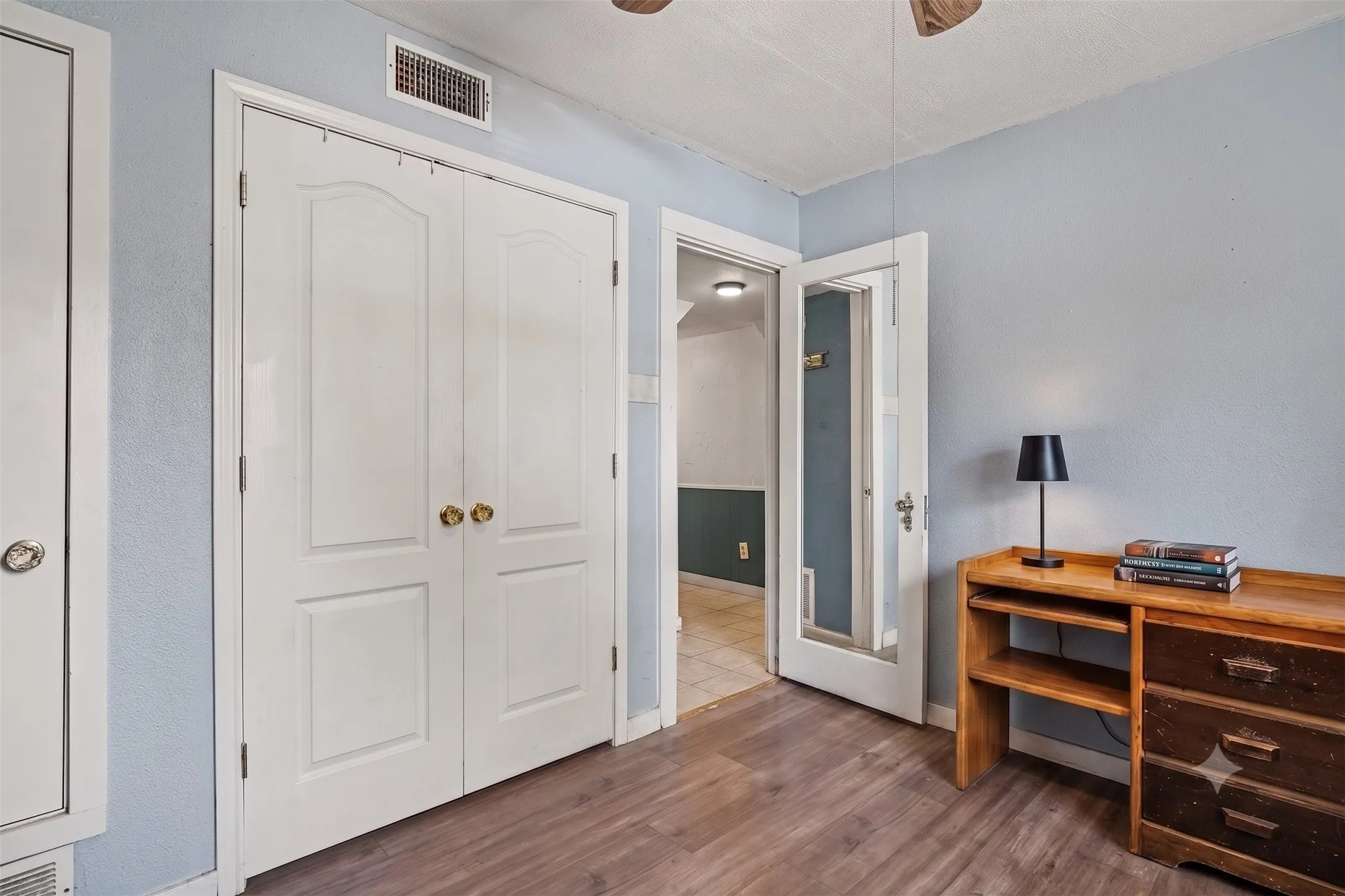 Versatile bedroom or home office space with wood-tone floors, double closet doors, and bright wall paint.