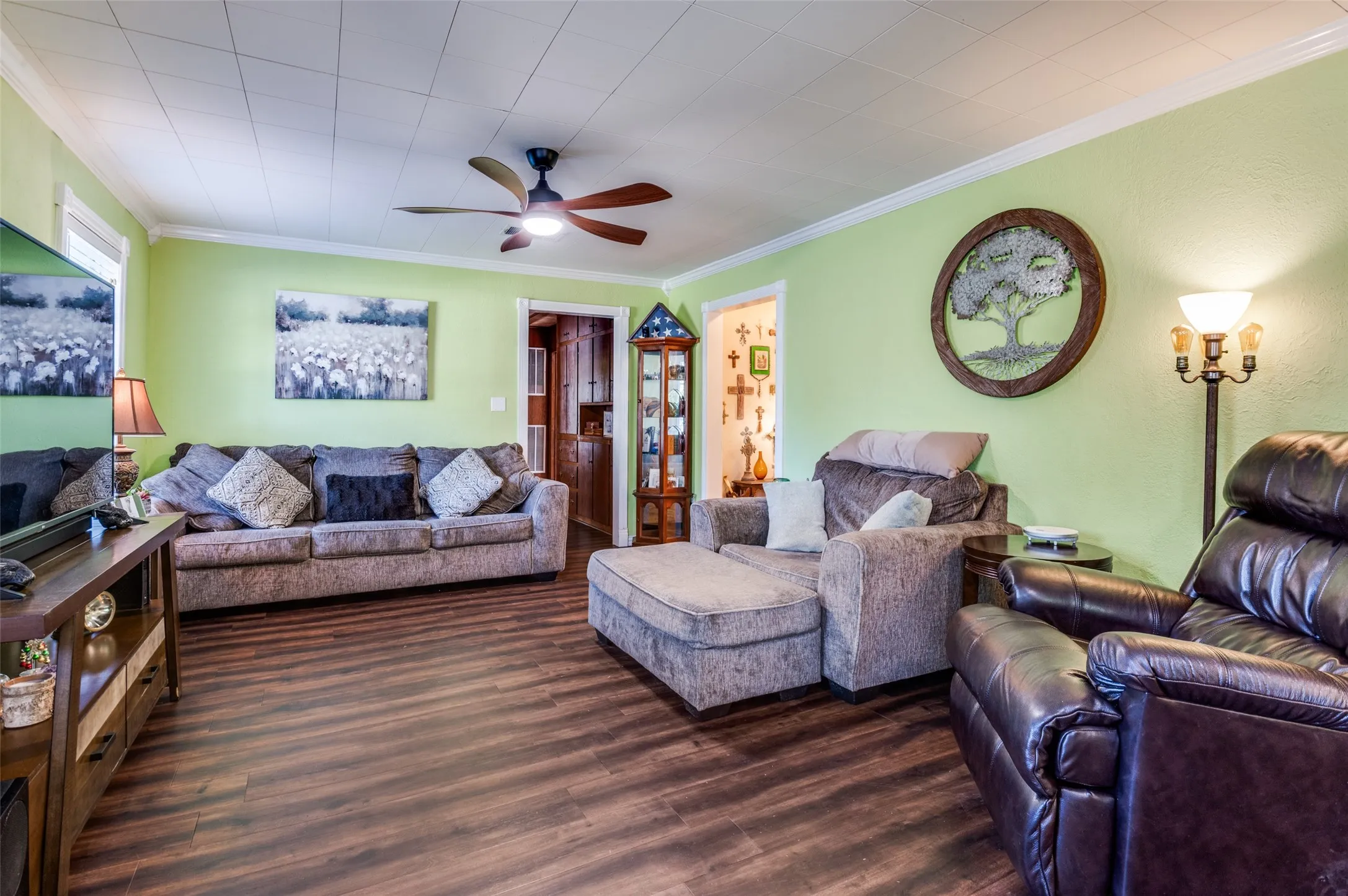 Wood-finish flooring, ceiling fan with integrated lighting, white crown molding, and light green wall finish