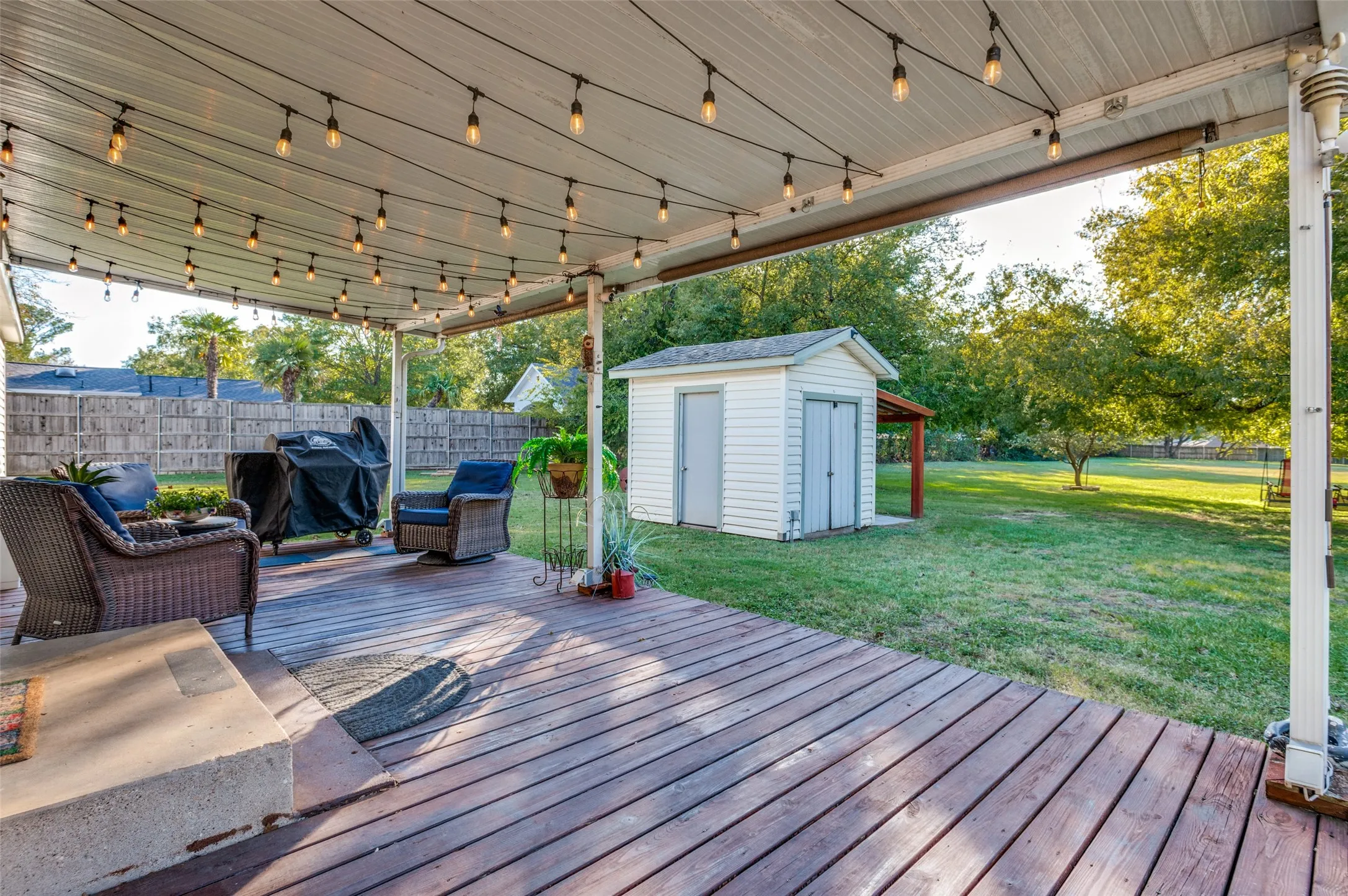 Expansive wood-finish deck with a covered patio, string lighting, and a substantial storage shed