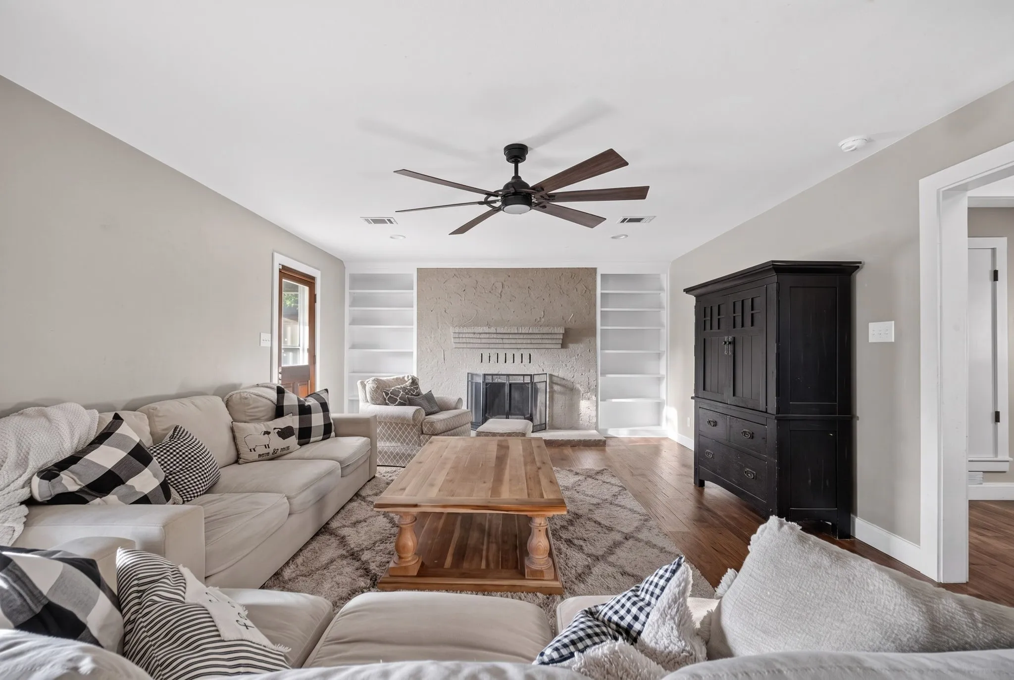 Hardwood-finish flooring, built-in shelving, fireplace with hearth, and a ceiling fan with integrated lighting