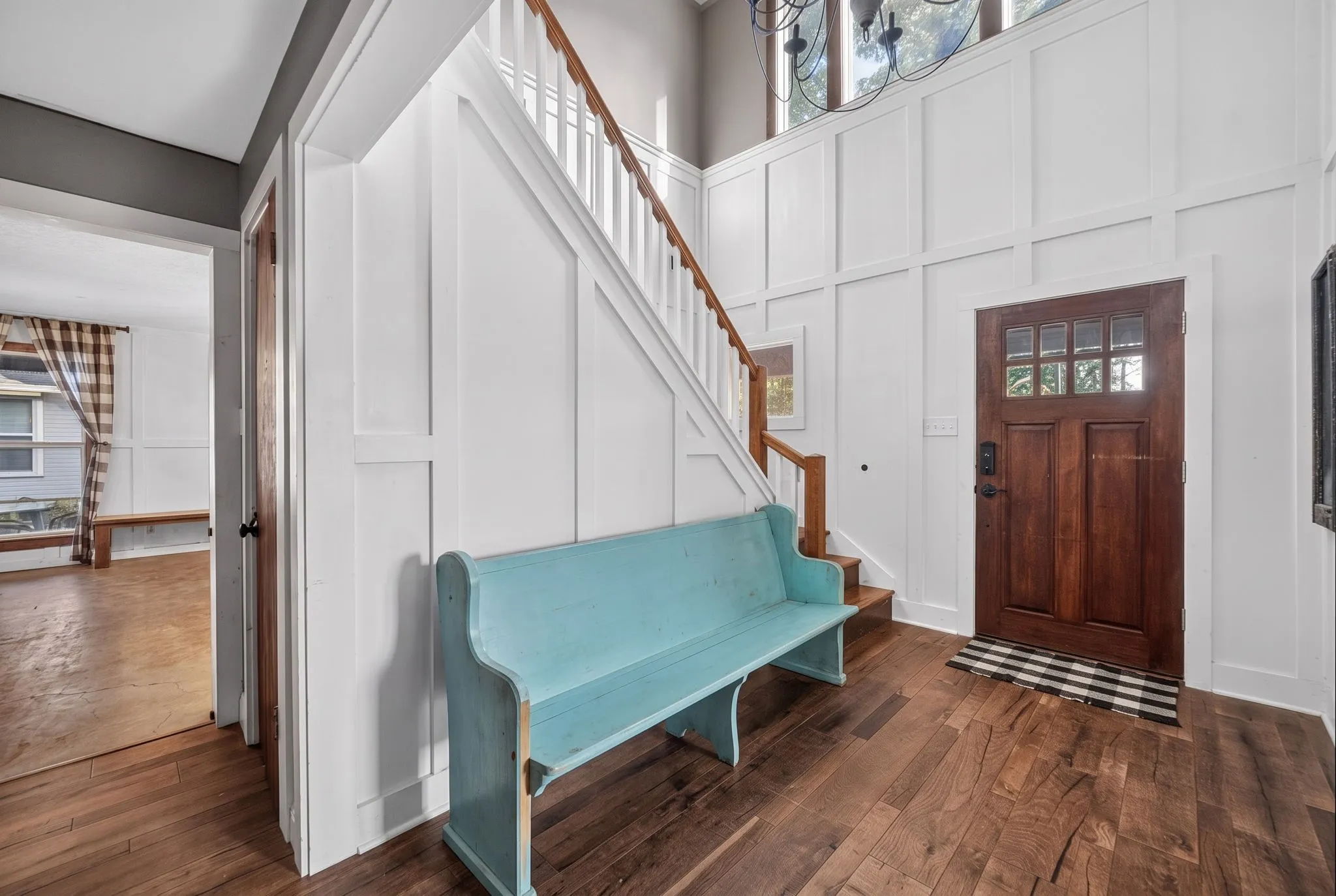 Hardwood flooring, white board and batten wall paneling, a wooden staircase with white balusters, a wooden front door with glass panels, and a two-story entry with upper windows