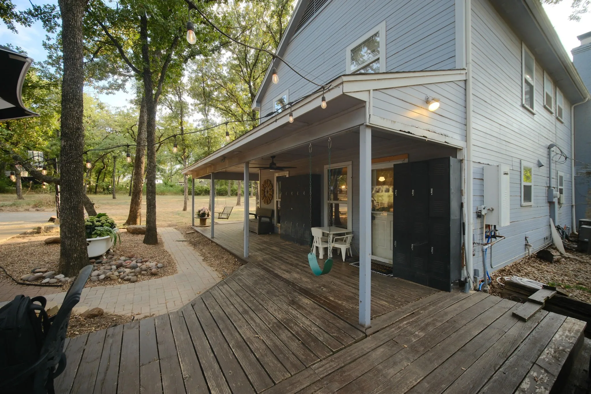 Expansive wooden deck leading to a covered porch, featuring a swing and string lighting