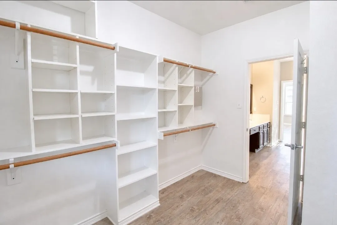 Spacious closet featuring multiple built-in shelving units, integrated hanging rods, and wood-finish flooring