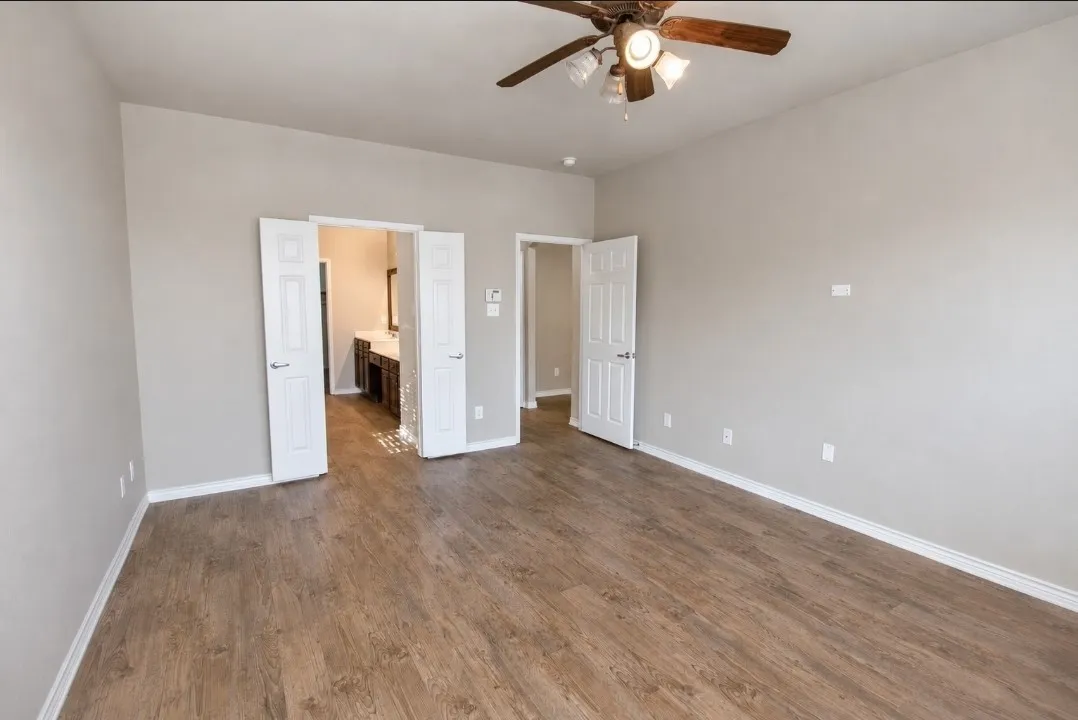 Spacious room featuring wood-finish flooring, light neutral wall tones, and a ceiling fan