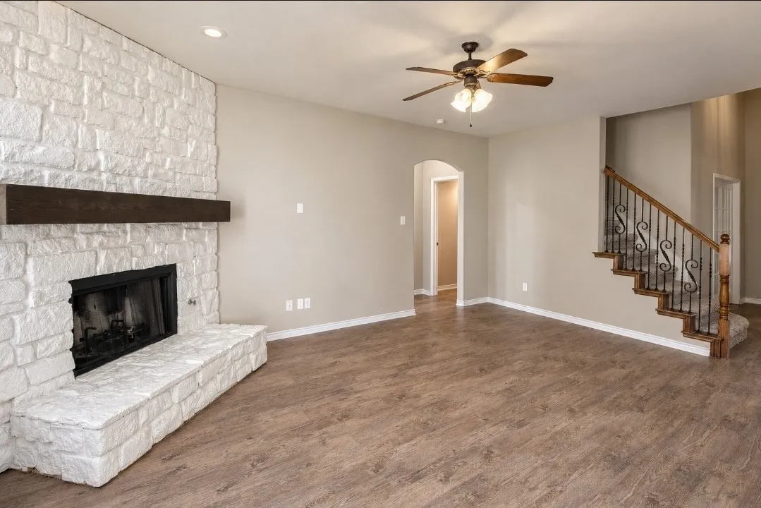 Stone-clad fireplace with a wood mantel, wood-finish flooring, staircase with wrought iron balusters, recessed lighting, and a ceiling fan