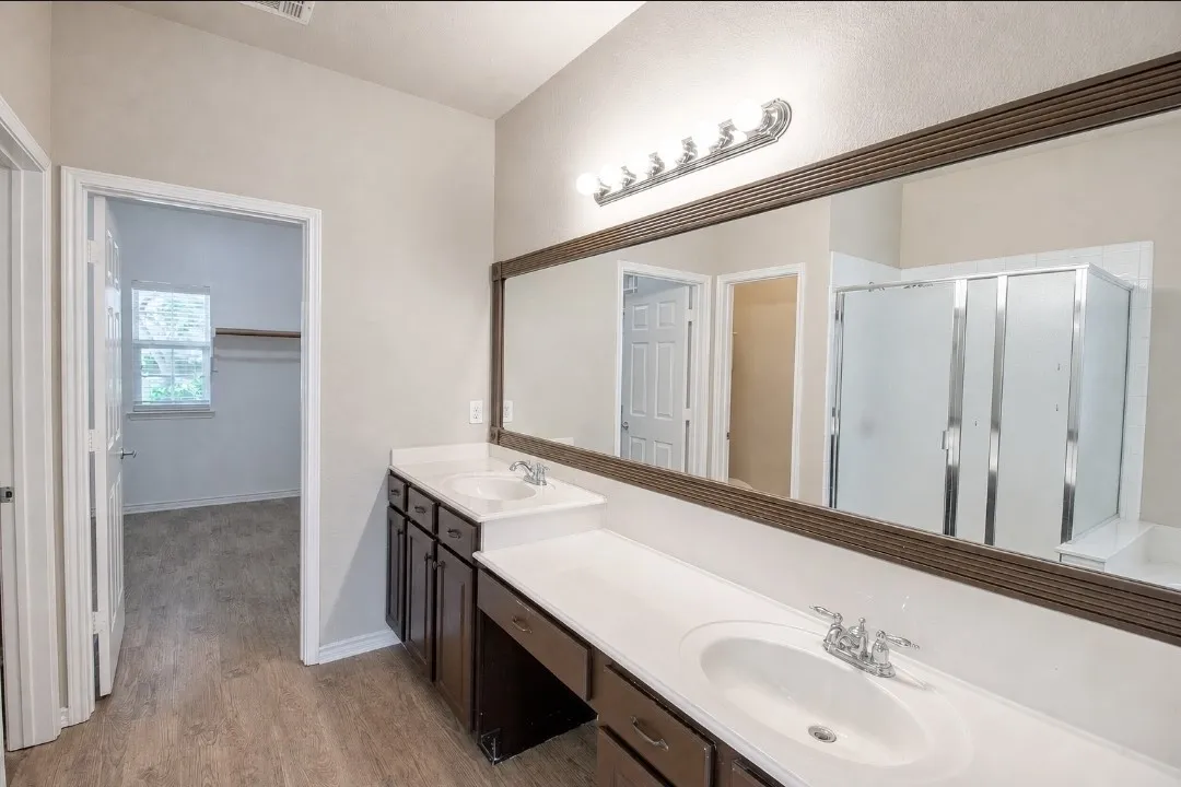 Double vanity with integrated sinks, dark wood-finish cabinetry, and expansive mirror